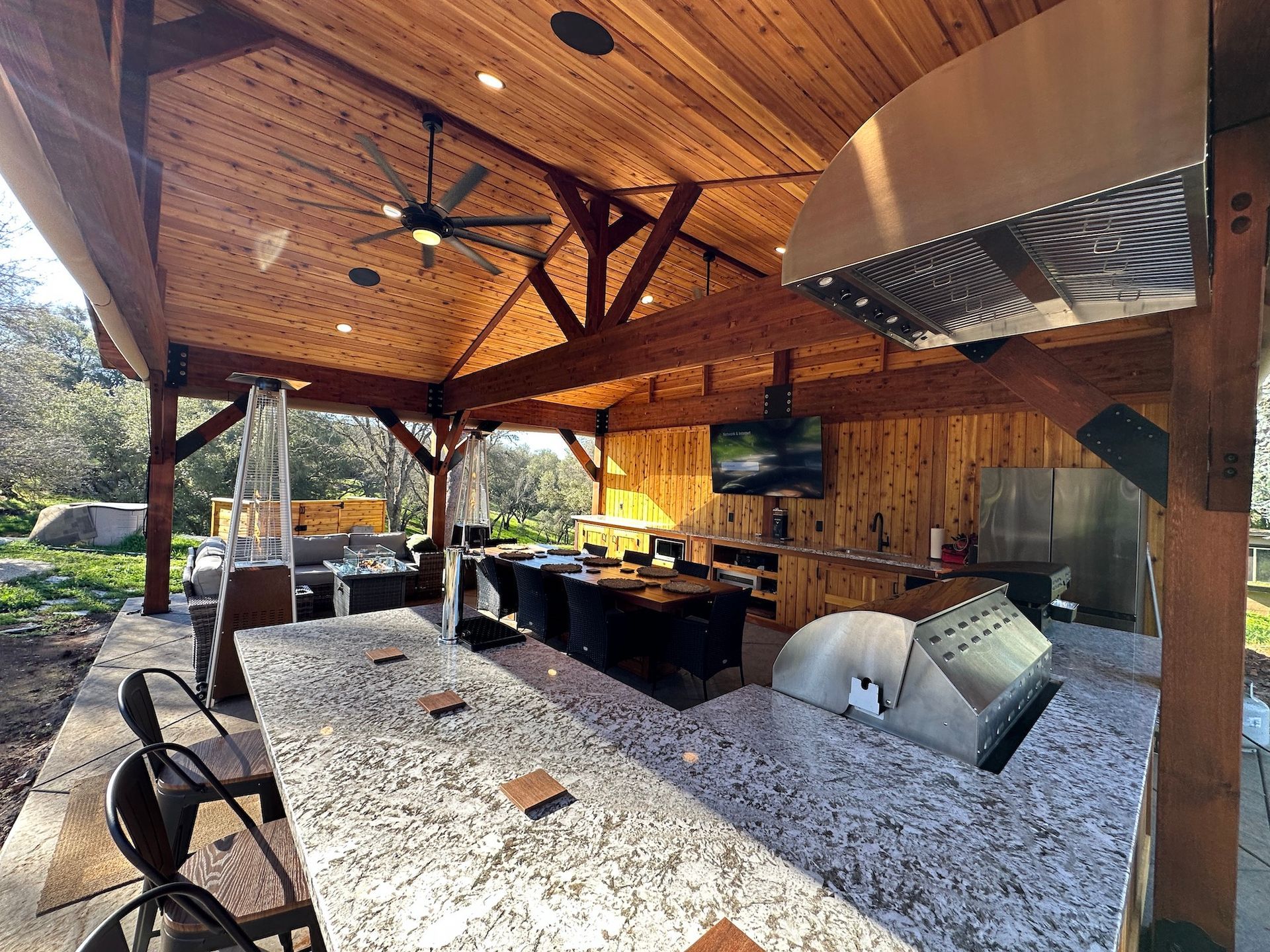 A large outdoor kitchen with a table and chairs under a wooden roof.