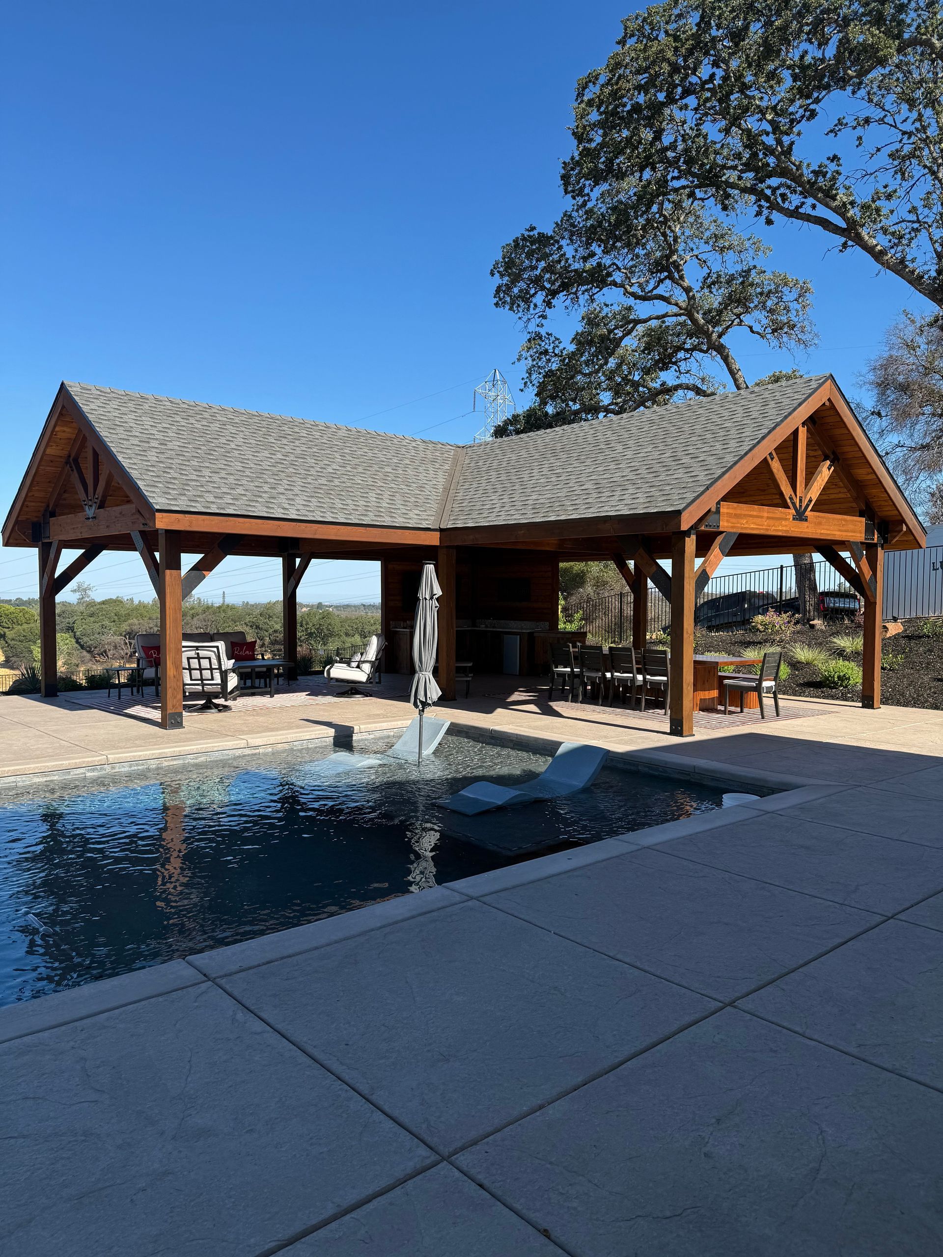 Poolside wooden pavilion with grey roof, overlooking a landscape.