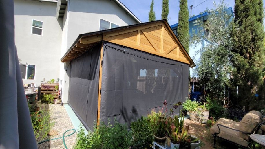 A shed with a screen on the side of it is in the backyard of a house.