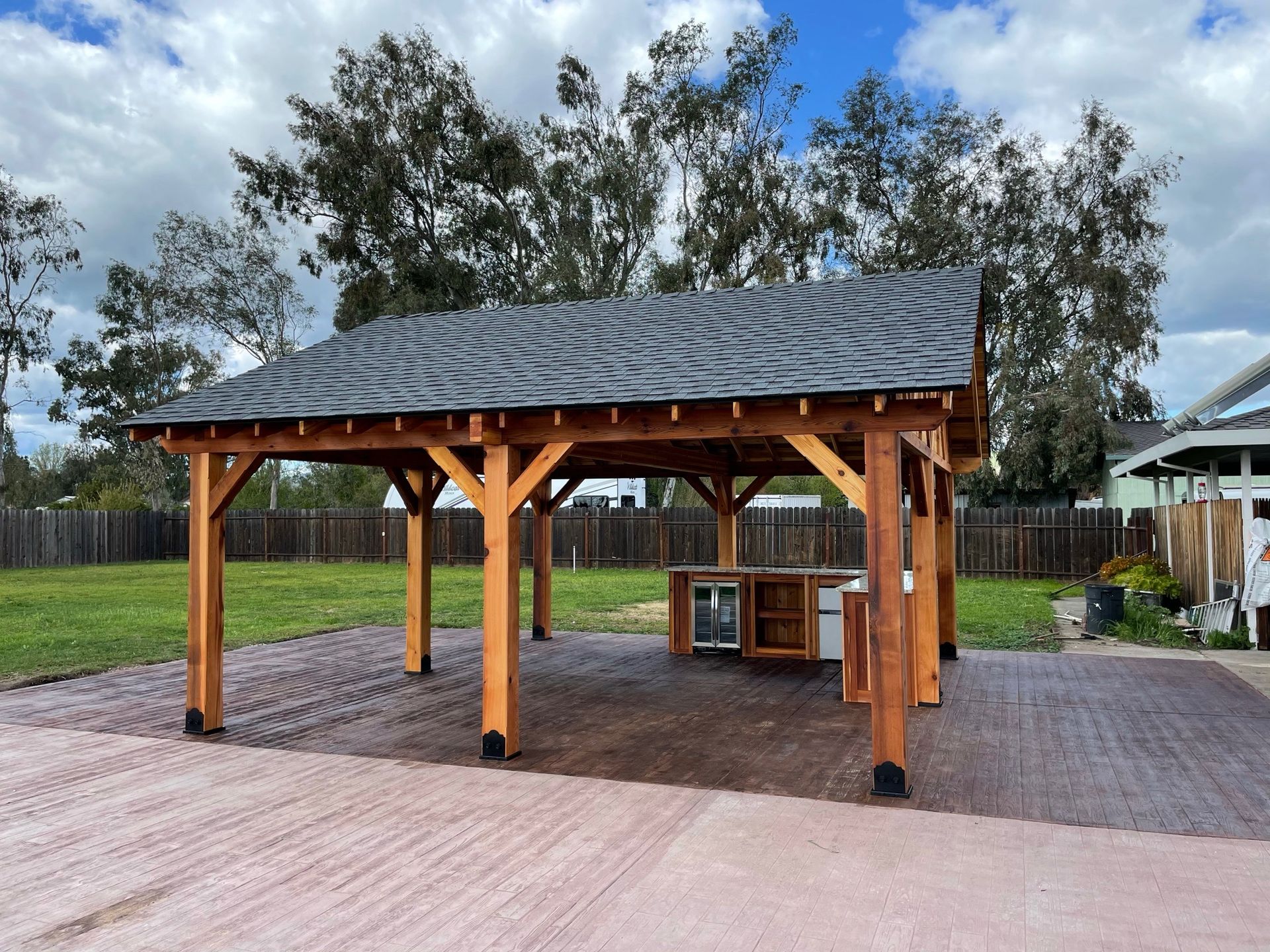 A large wooden pavilion with a slate roof in a backyard.