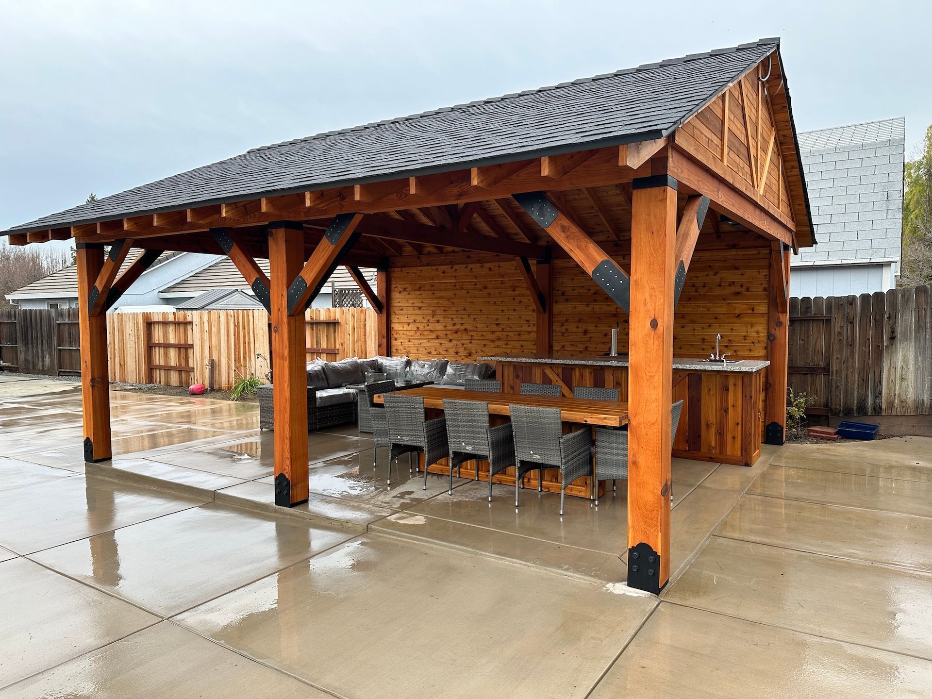 A large wooden pavilion with a table and chairs underneath it.