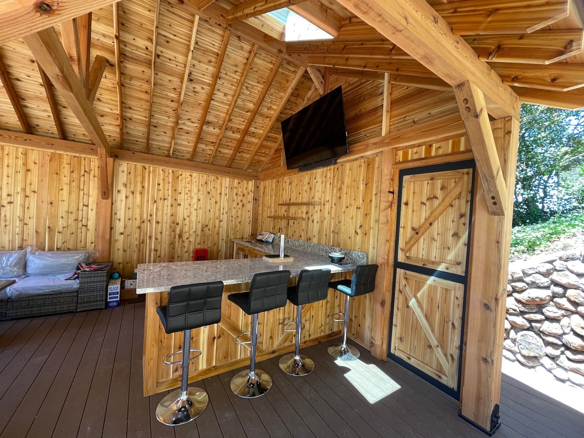 A wooden gazebo with a bar , chairs , and a flat screen tv.