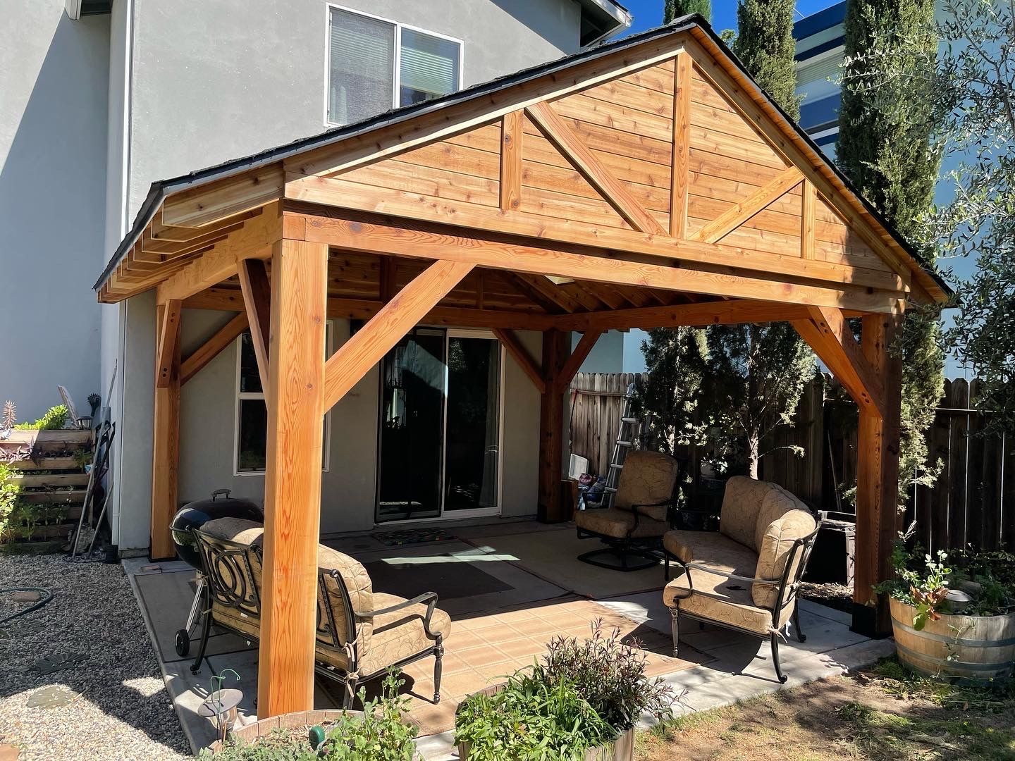 A wooden pavilion with a roof is in the backyard of a house.