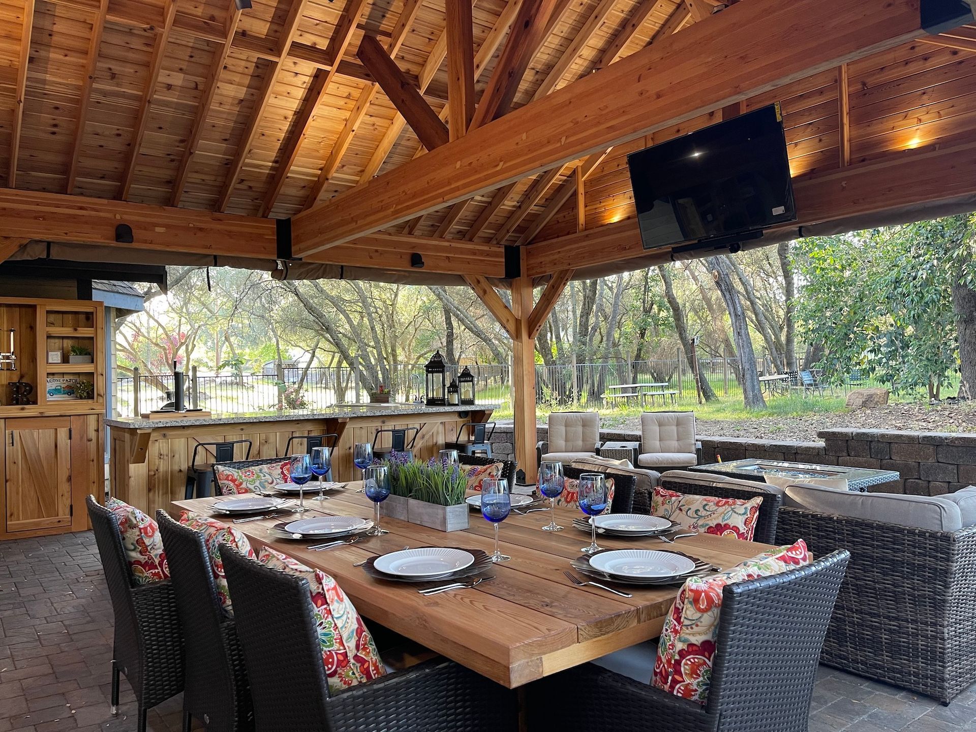 A large wooden table and chairs under a wooden roof.