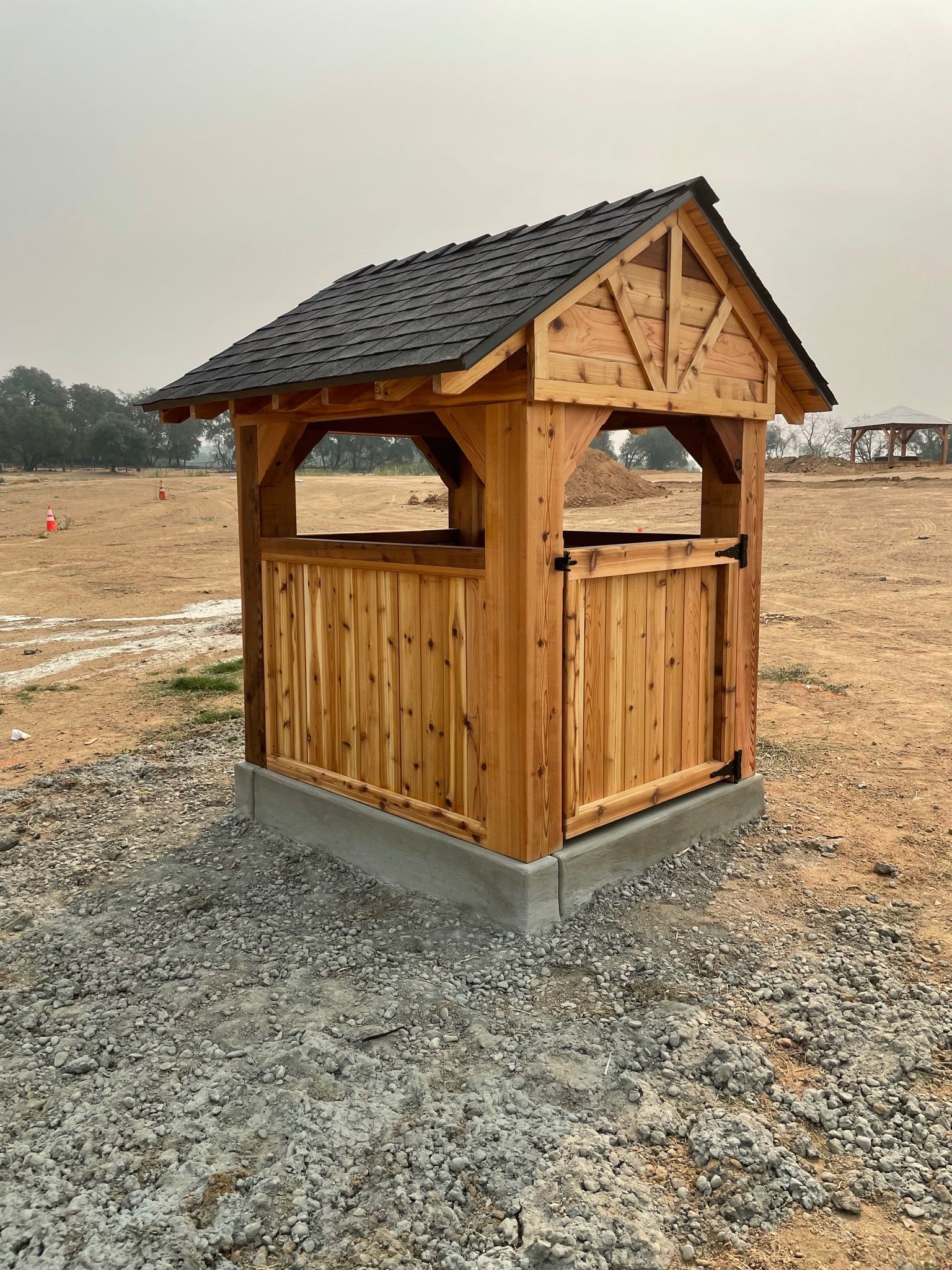 A small wooden shed is sitting in the middle of a gravel field.