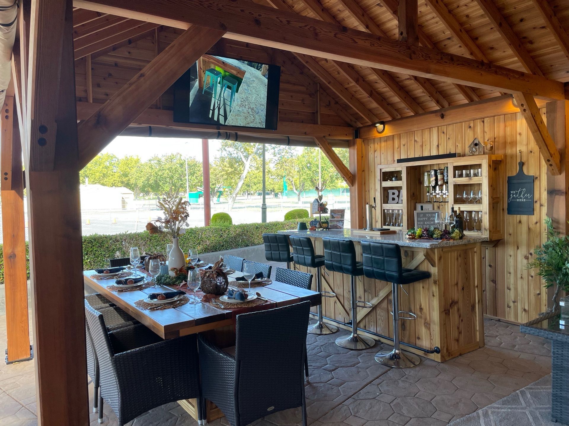A wooden gazebo with a dining table and chairs and a bar.