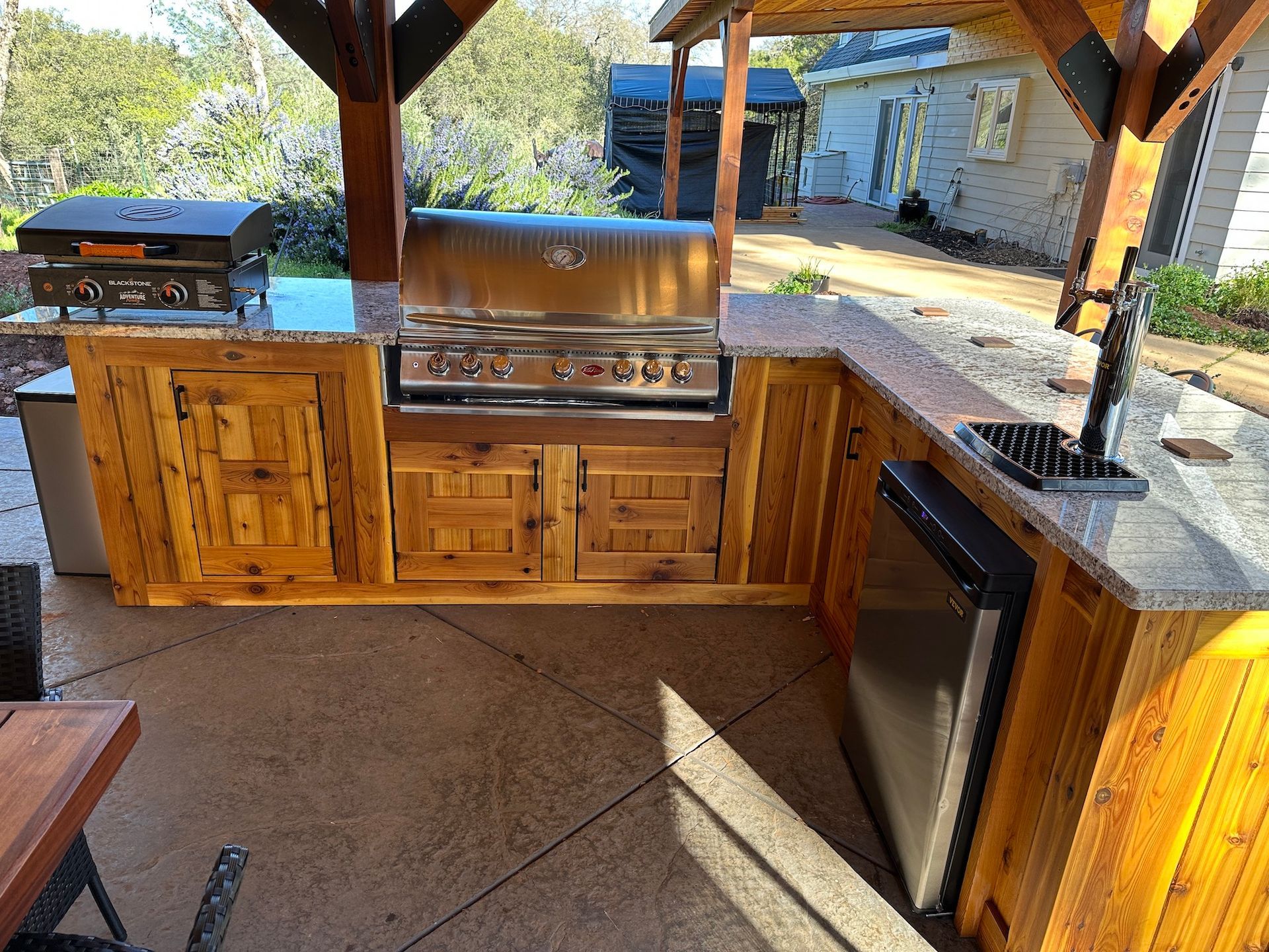 A wooden outdoor kitchen with a grill and a refrigerator.