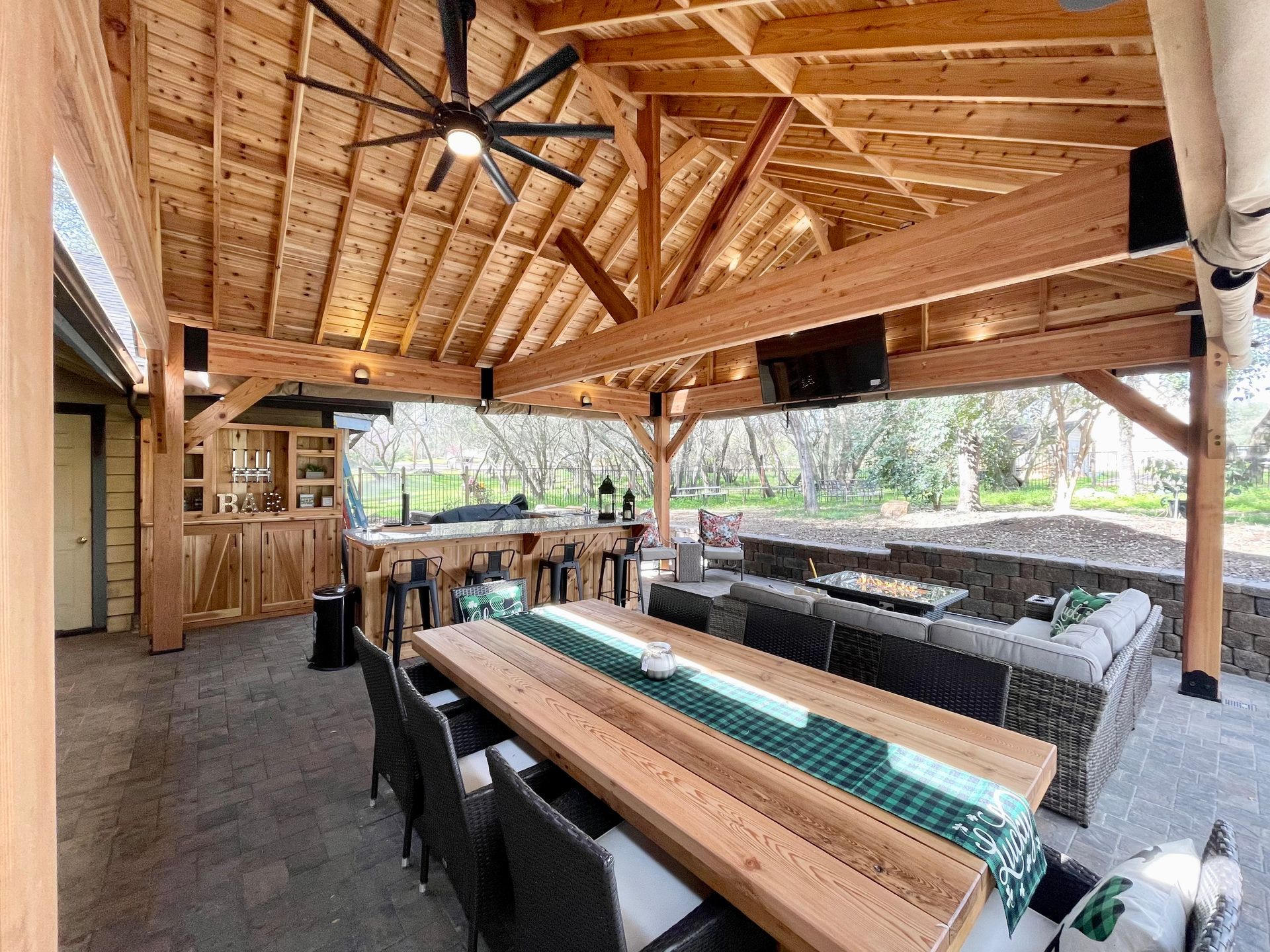 A large wooden table and chairs under a wooden roof.