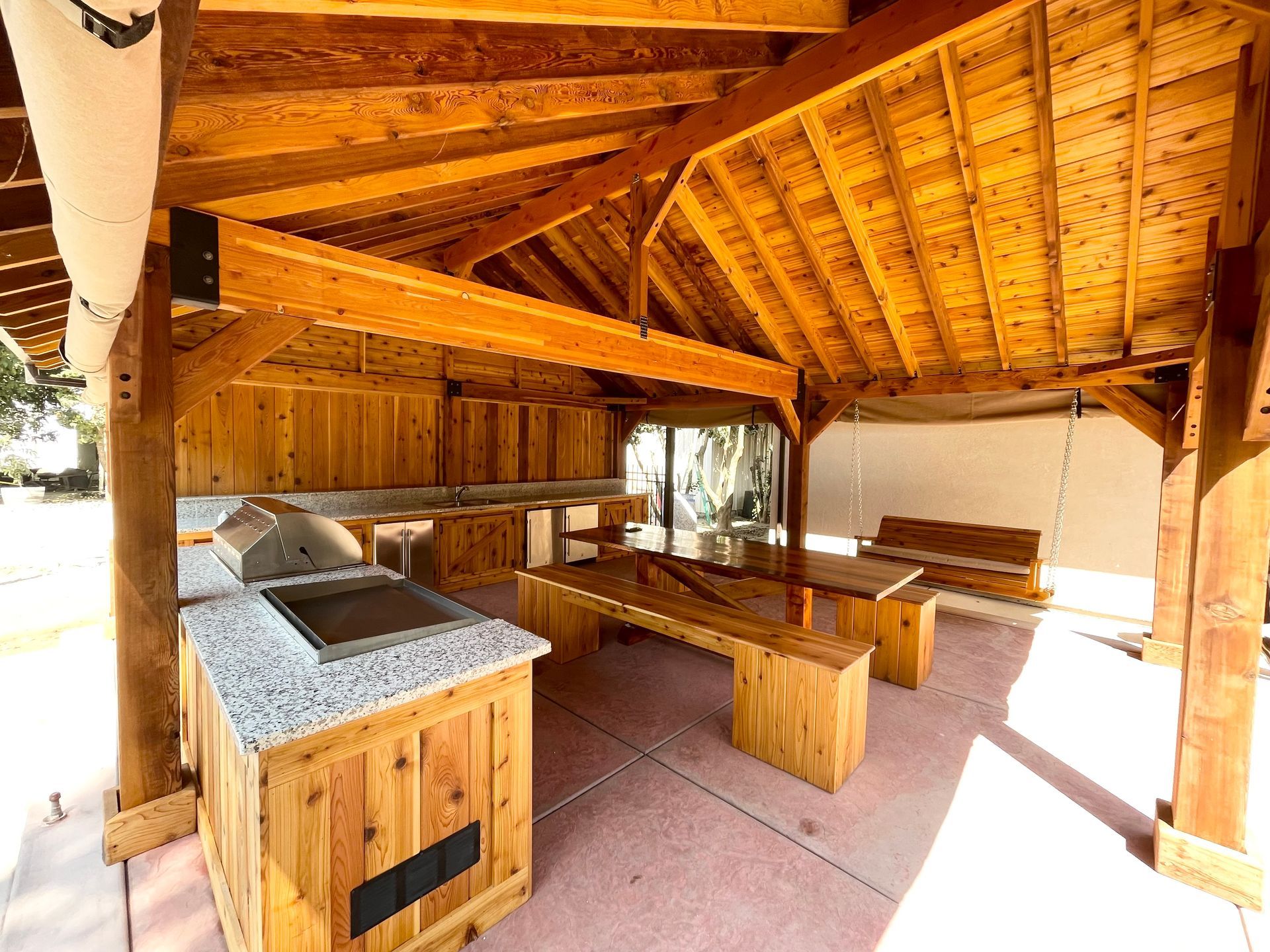 A wooden pavilion with a table and benches under a wooden roof.