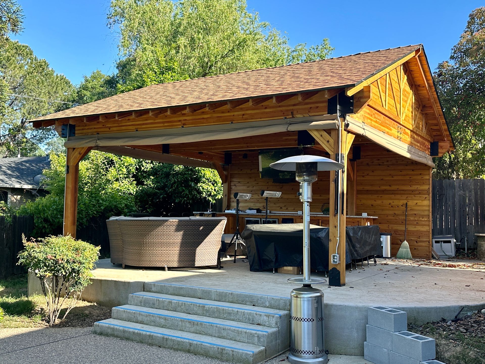 A wooden pavilion with a patio area and a heater in front of it.