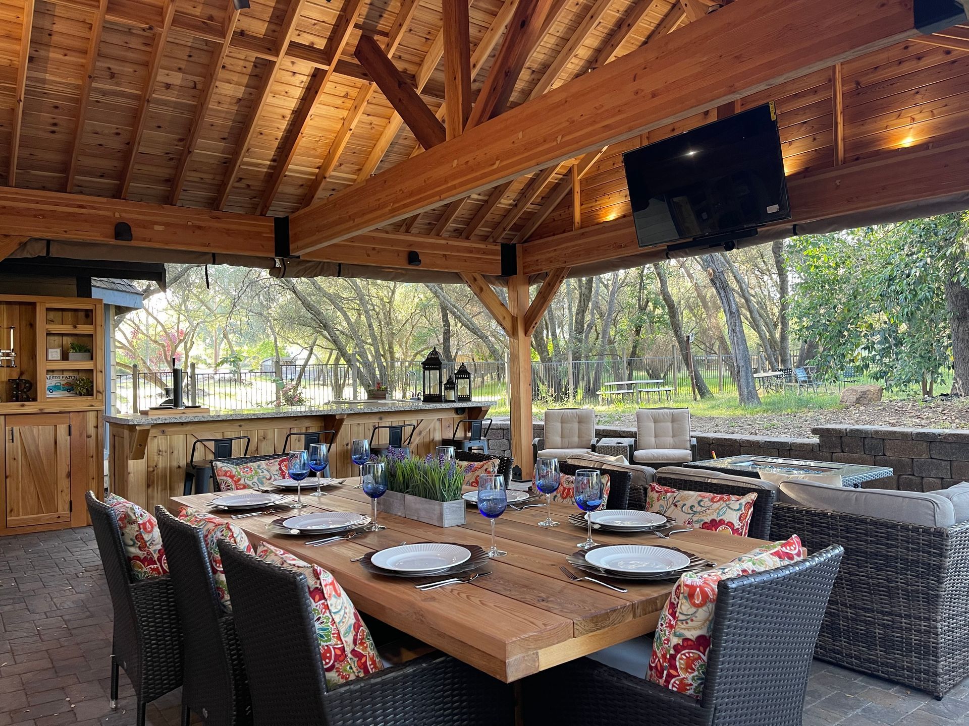 A large wooden table and chairs under a wooden roof.