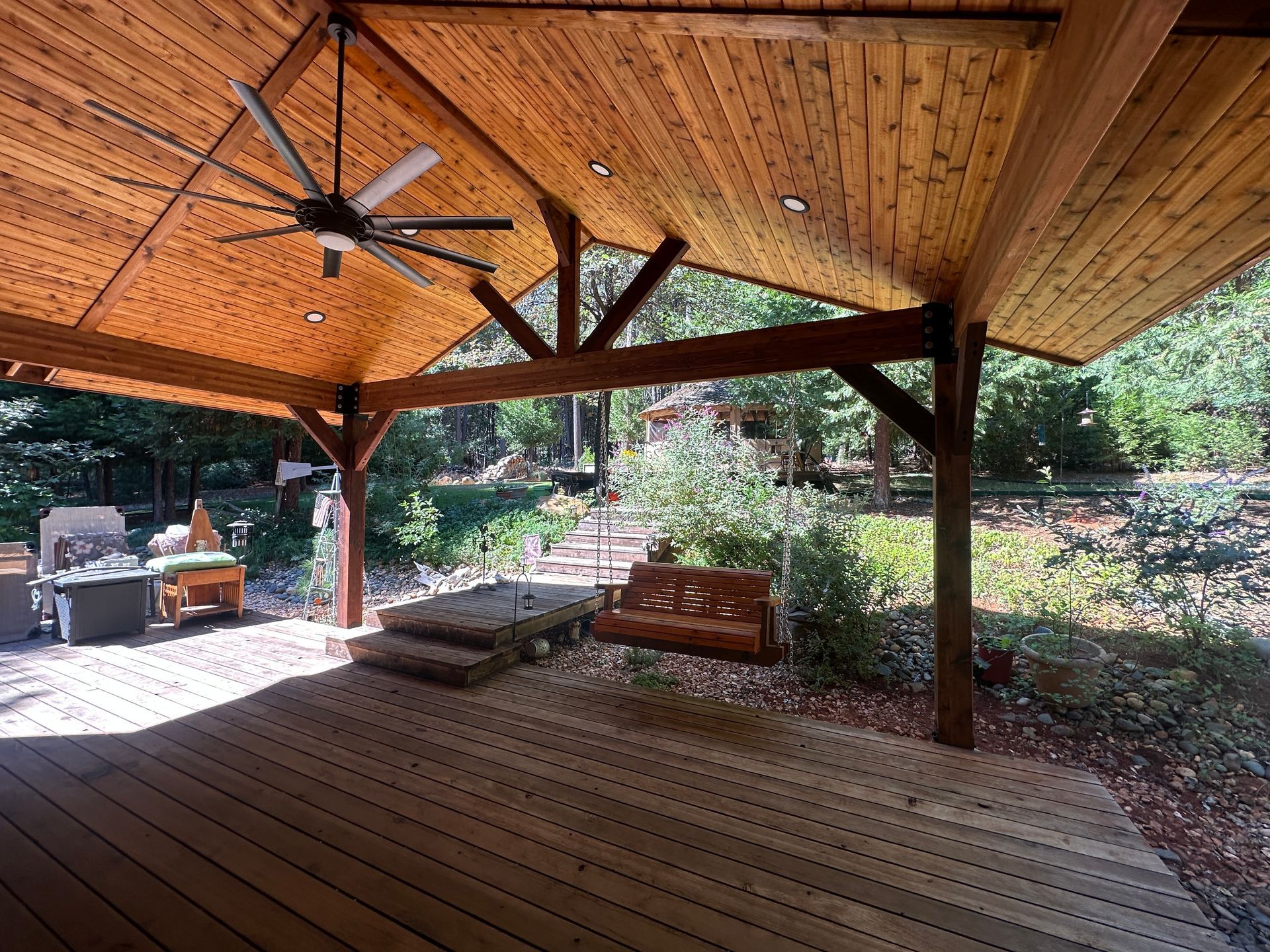 A wooden deck with a ceiling fan and a swing.