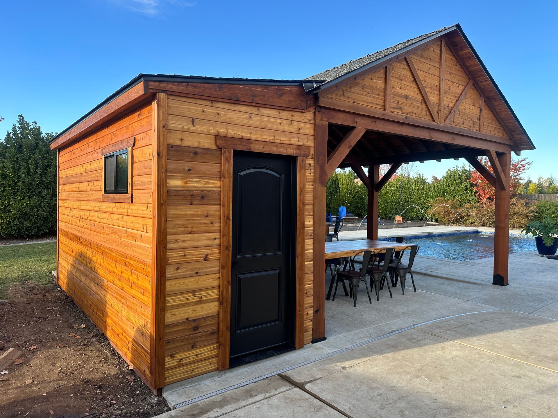 A wooden shed with a pavilion attached to it is next to a pool.