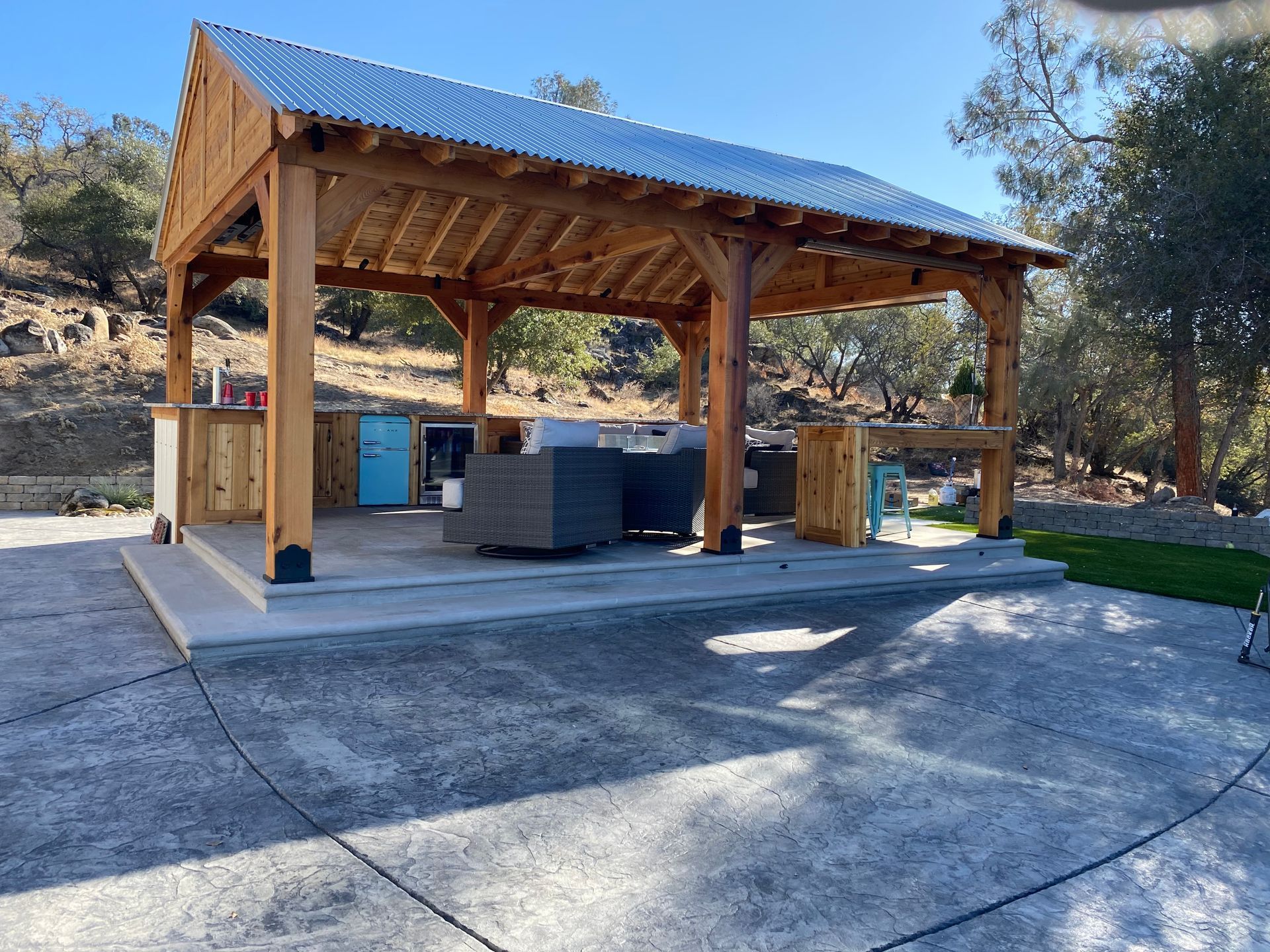 A wooden pavilion with a metal roof is sitting on top of a concrete patio.