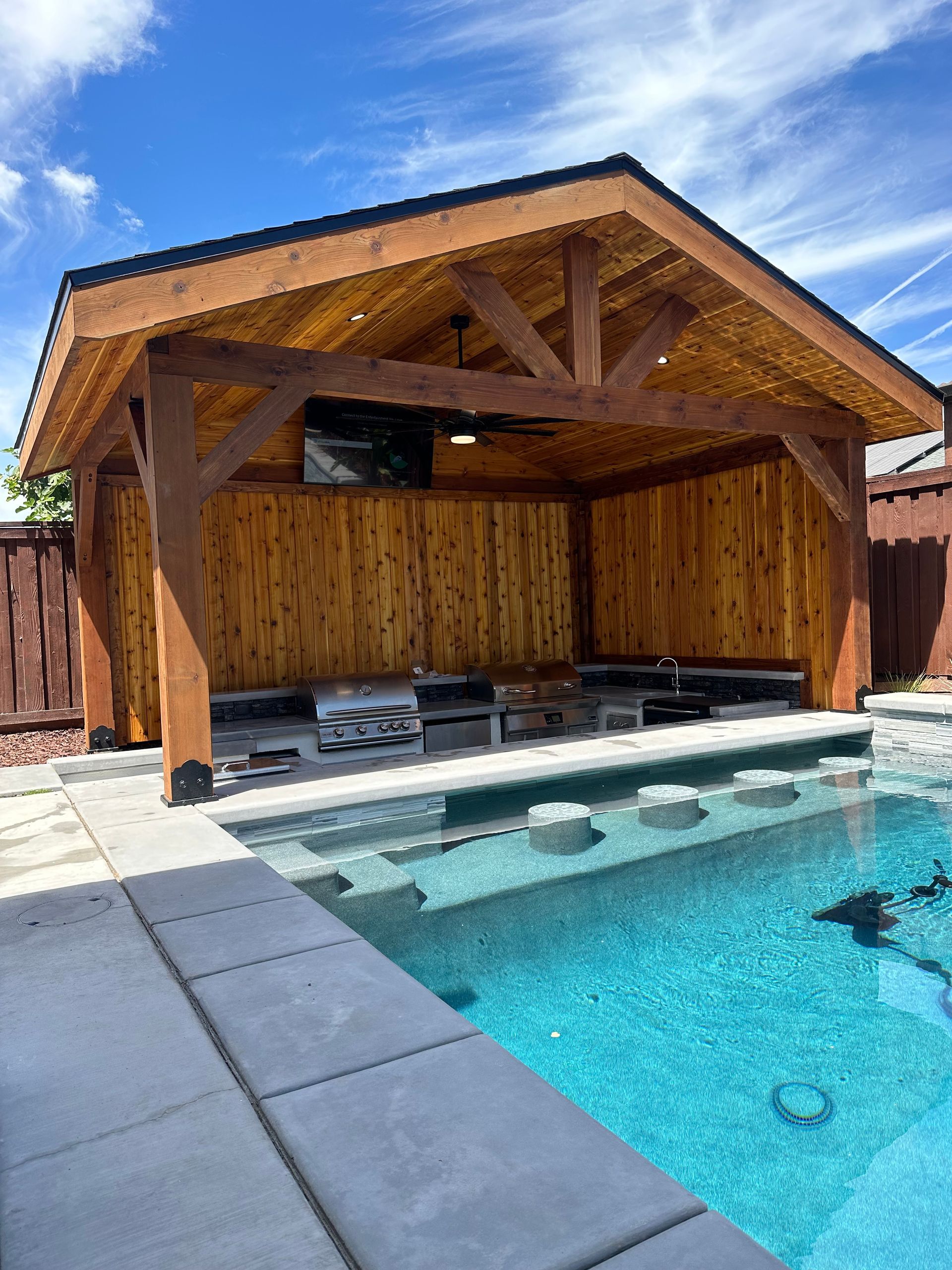 A wooden pavilion with a swimming pool in front of it.