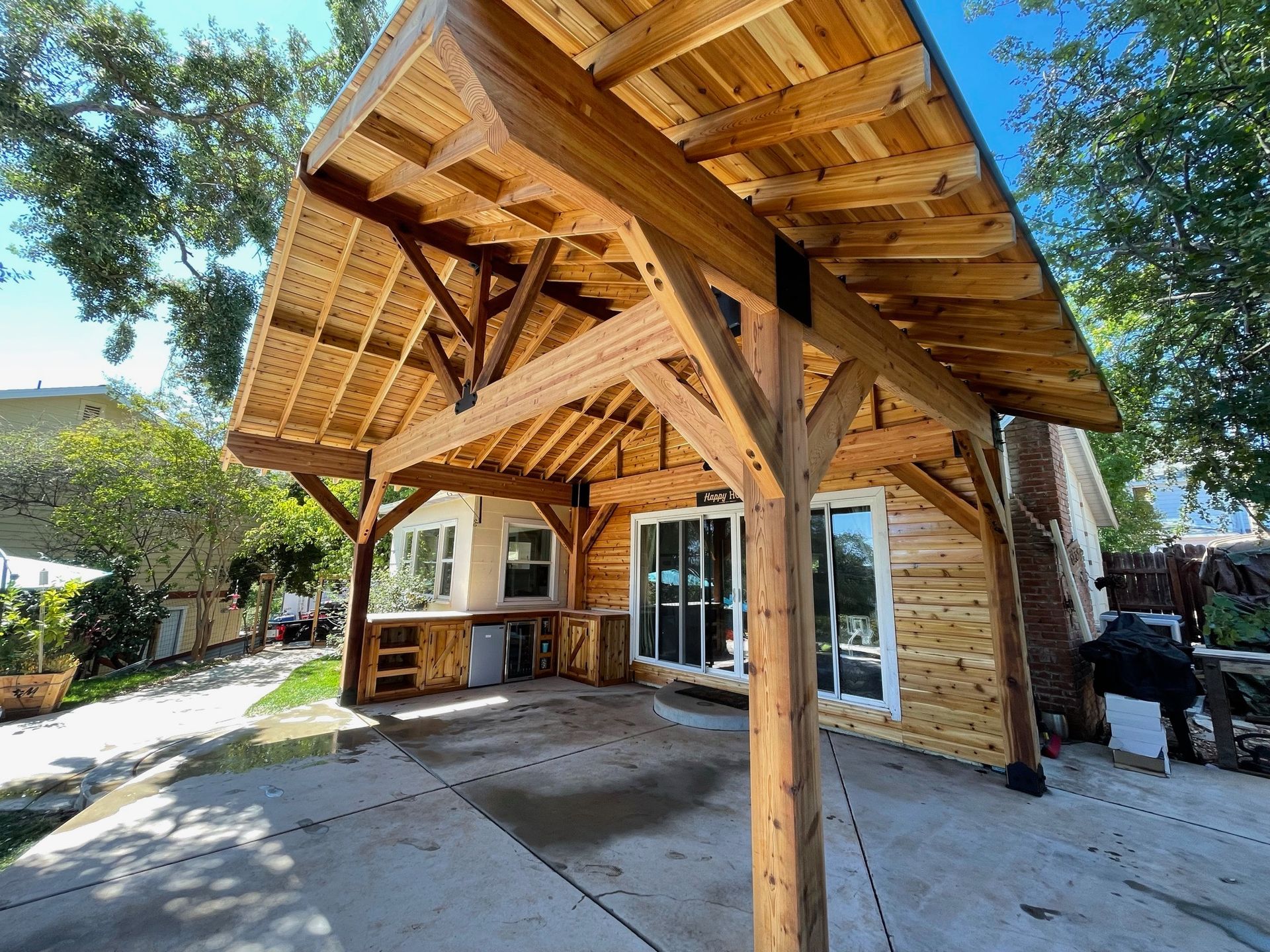 A wooden structure with a roof over a patio in front of a house.