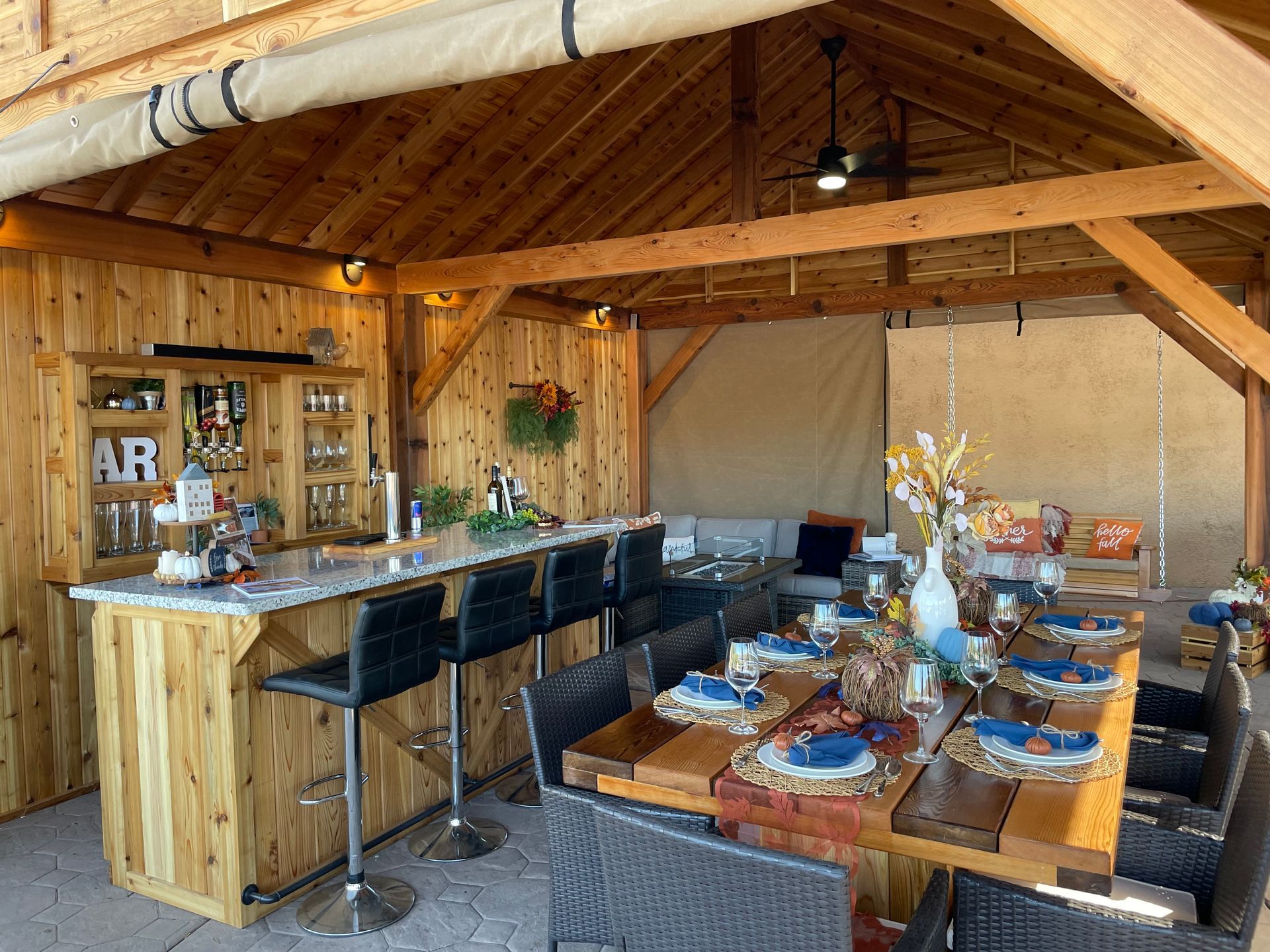A wooden pavilion with a table and chairs and a bar.