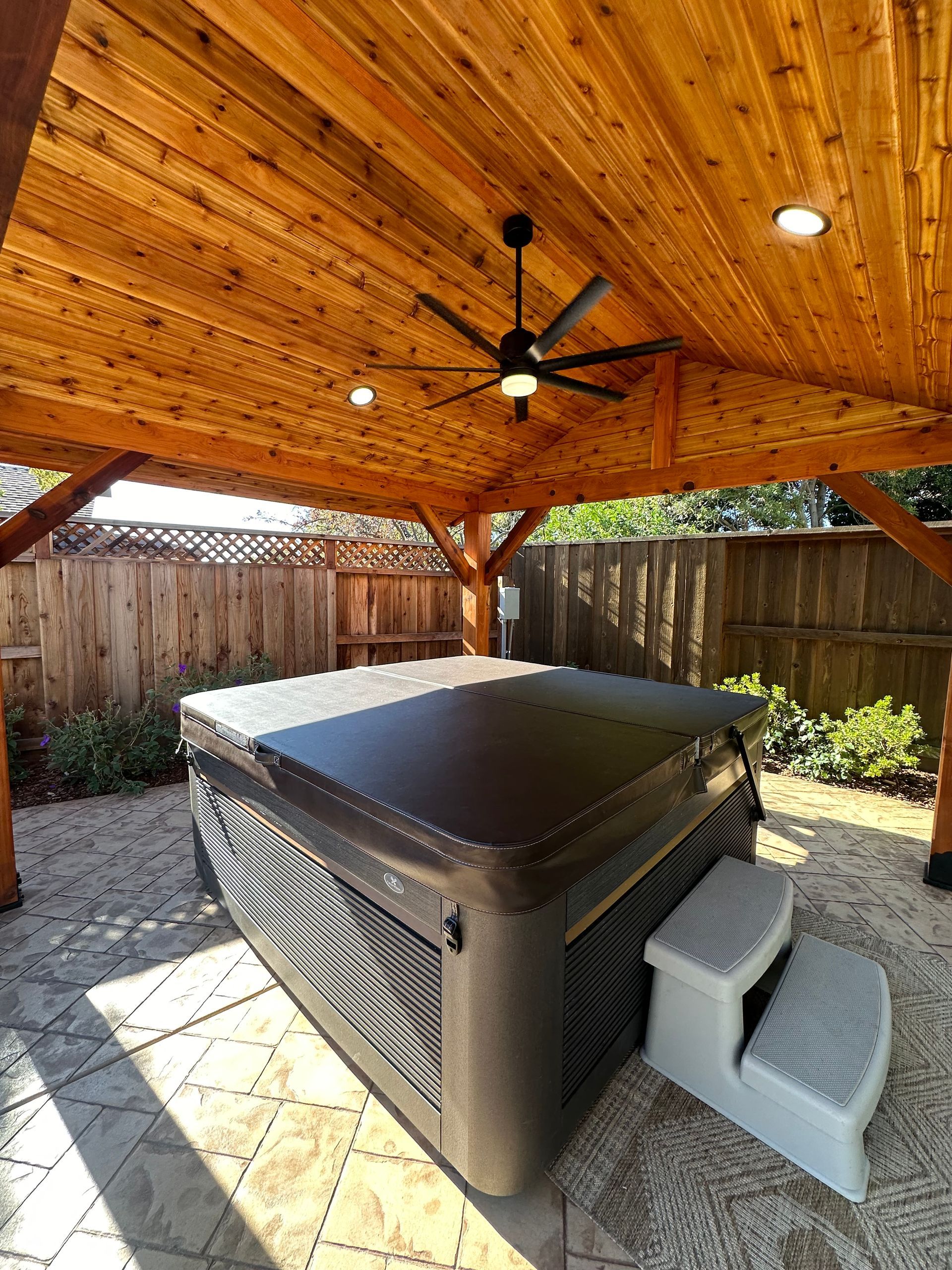 A hot tub is under a wooden structure with a ceiling fan.