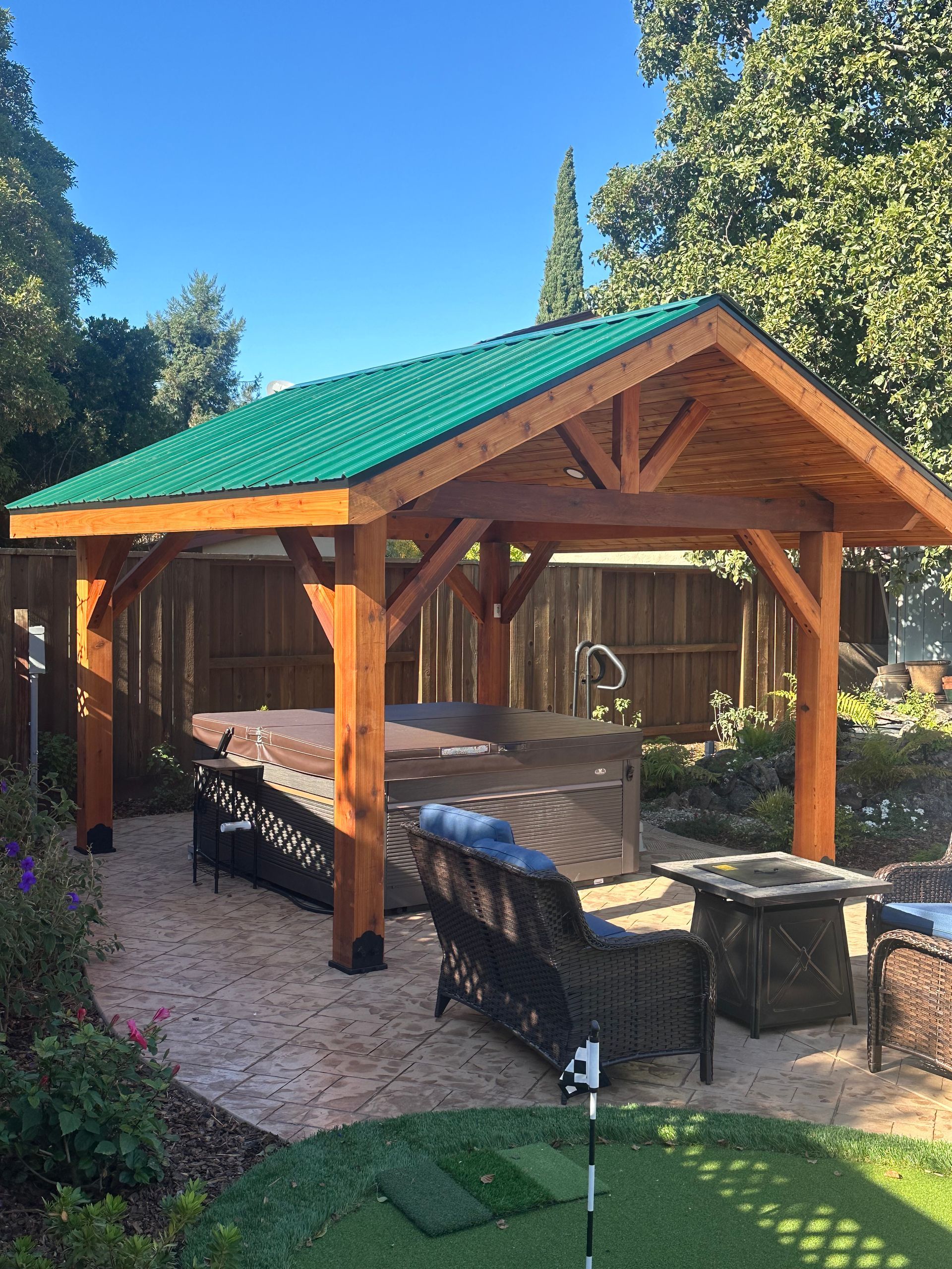 A wooden pavilion with a green roof in a backyard.