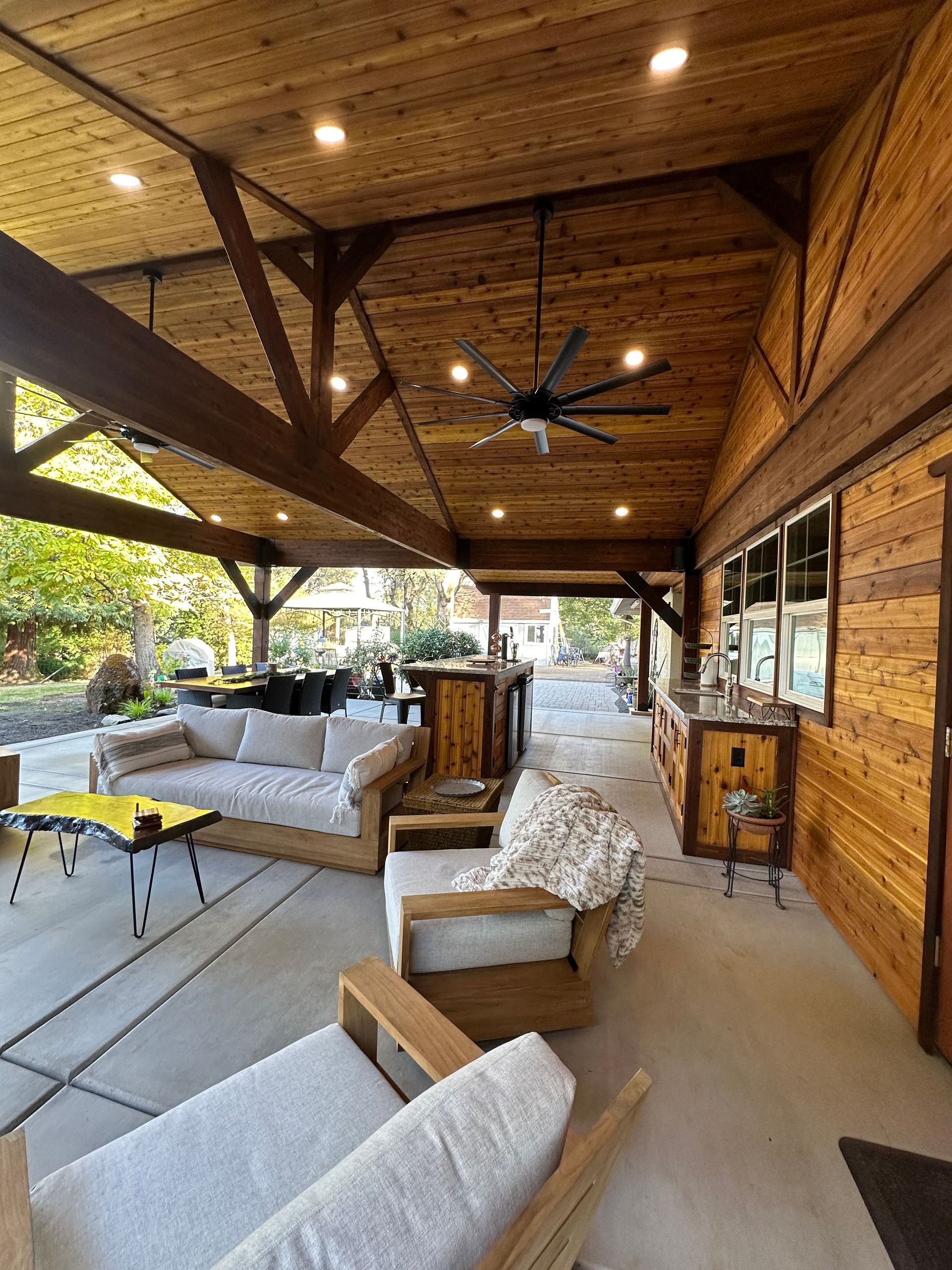 A covered patio with a couch , chairs , and a ceiling fan.