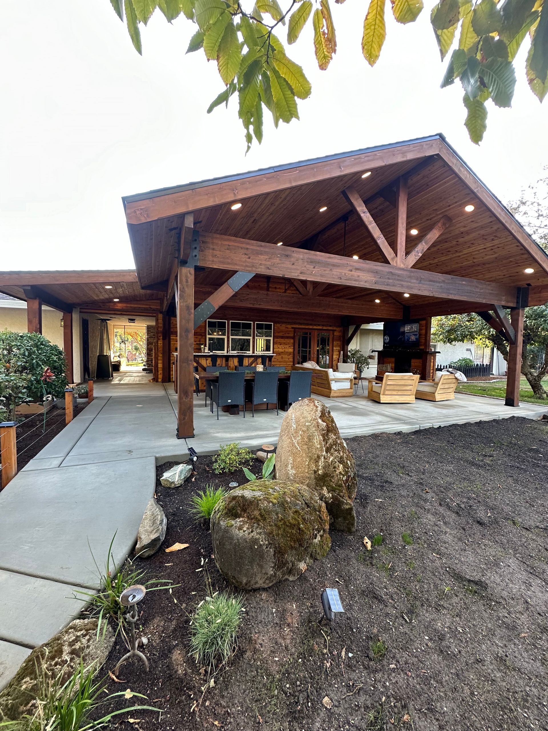 A large wooden house with a covered patio and a large rock in front of it.