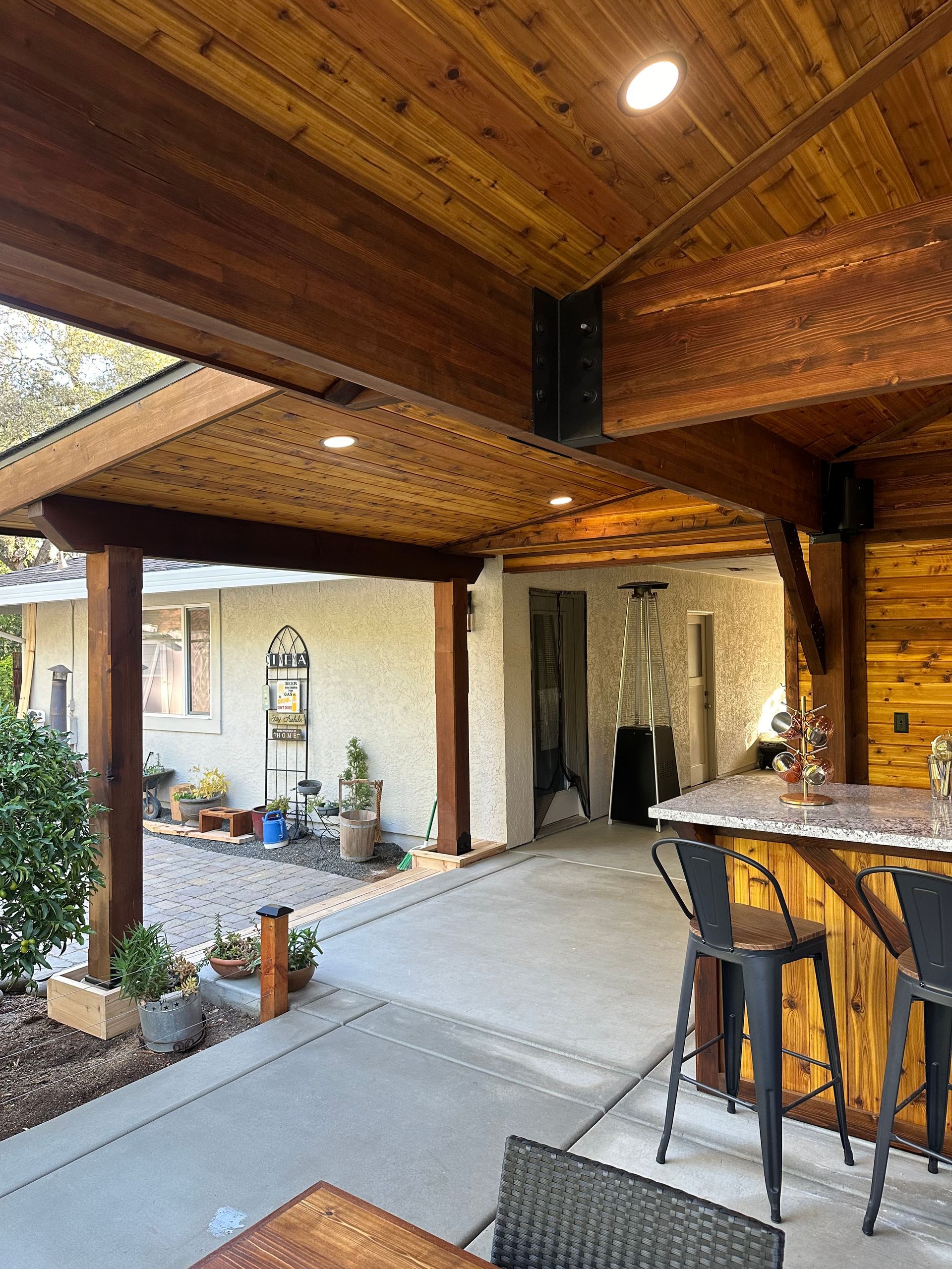 A wooden patio with a table and chairs under a wooden roof.