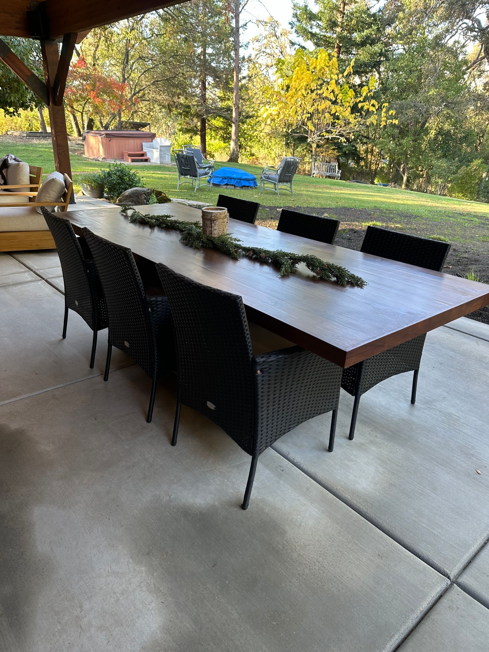 A long table with chairs on a patio with trees in the background.