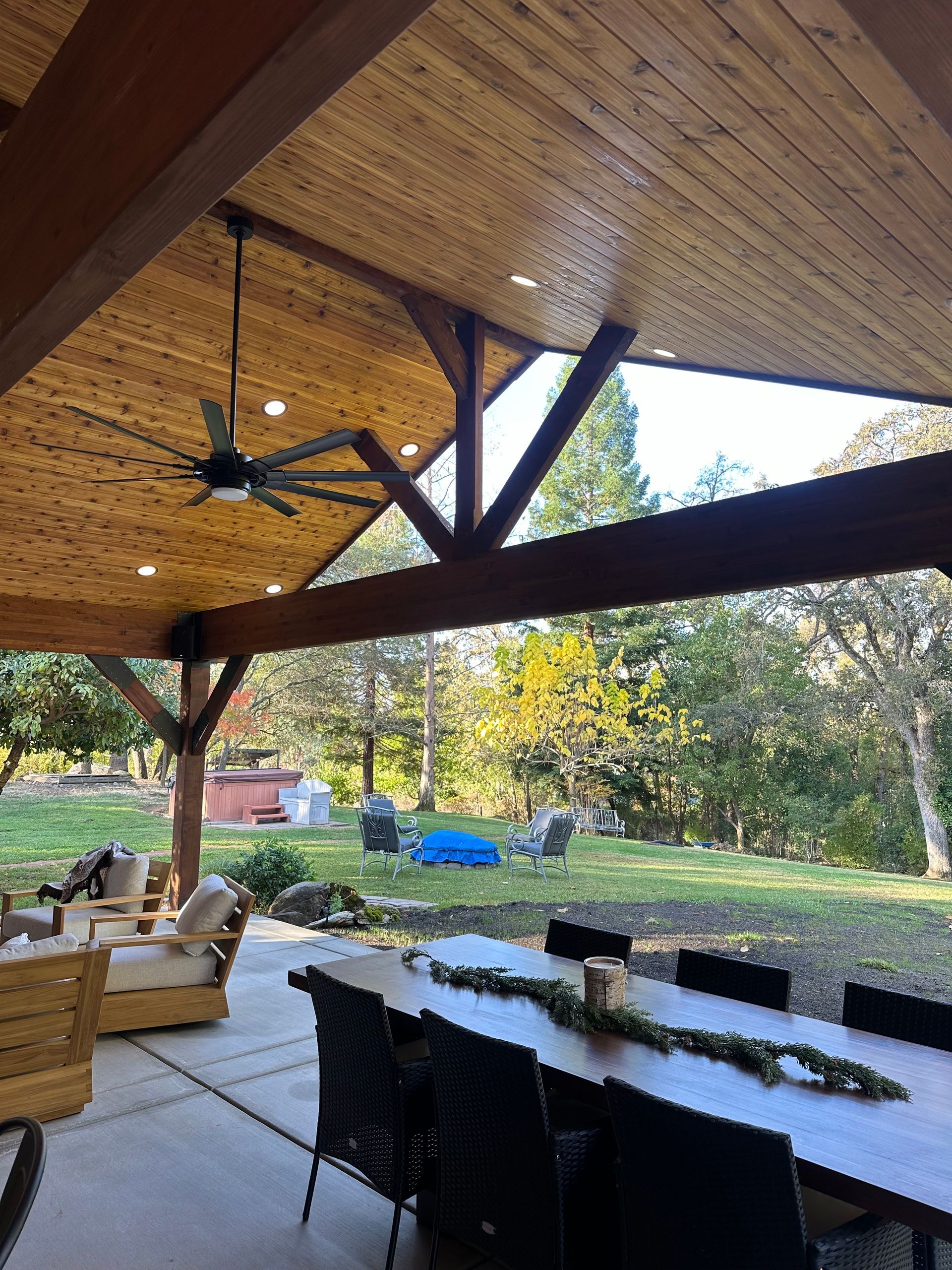 A patio with a table and chairs under a wooden ceiling with a ceiling fan.