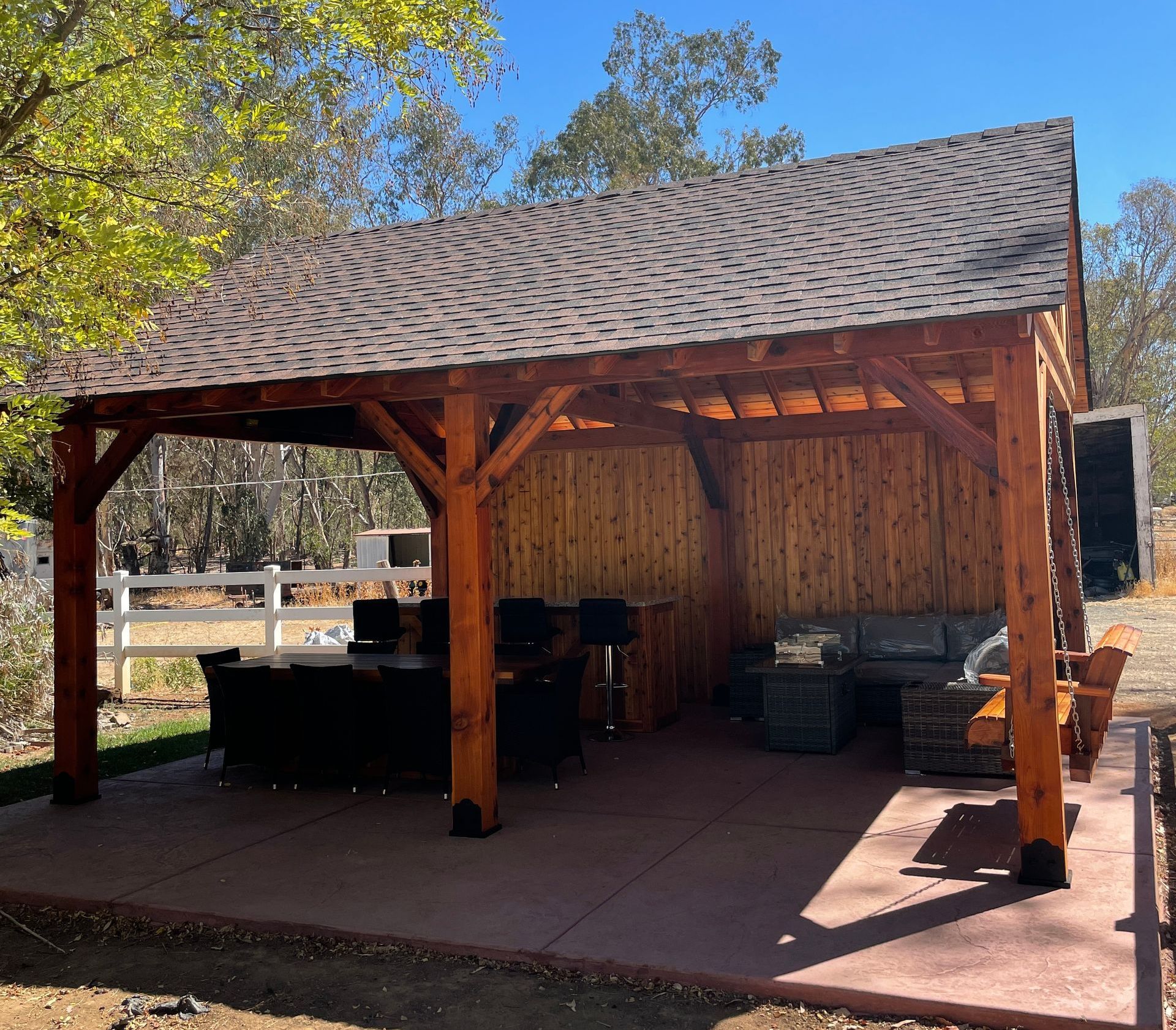 A large wooden pavilion with a couch and chairs underneath it