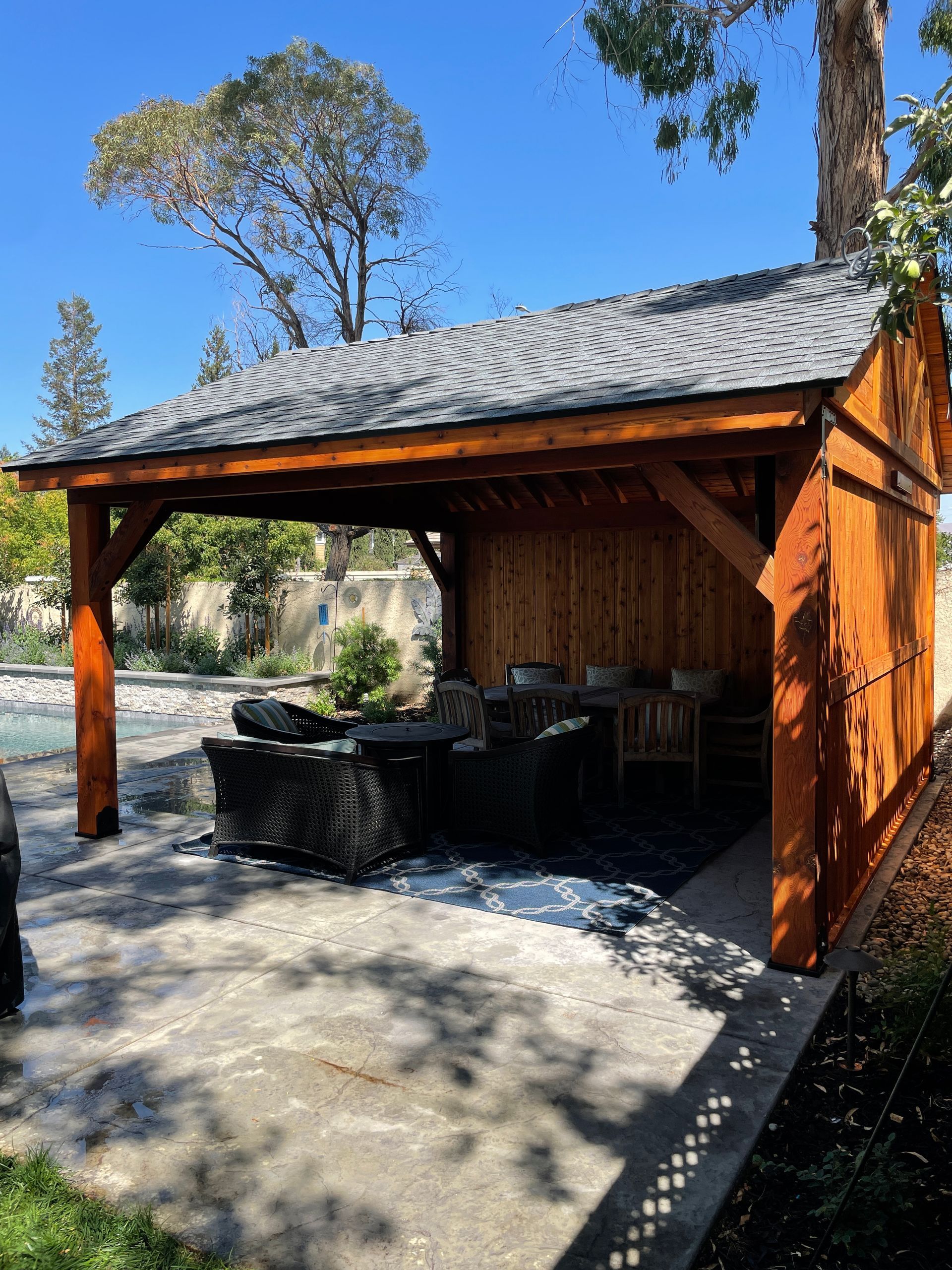 A wooden pavilion with a gray roof is sitting next to a pool.