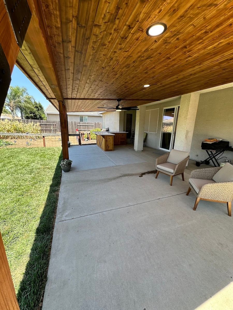 A patio with a wooden ceiling and chairs and a table.