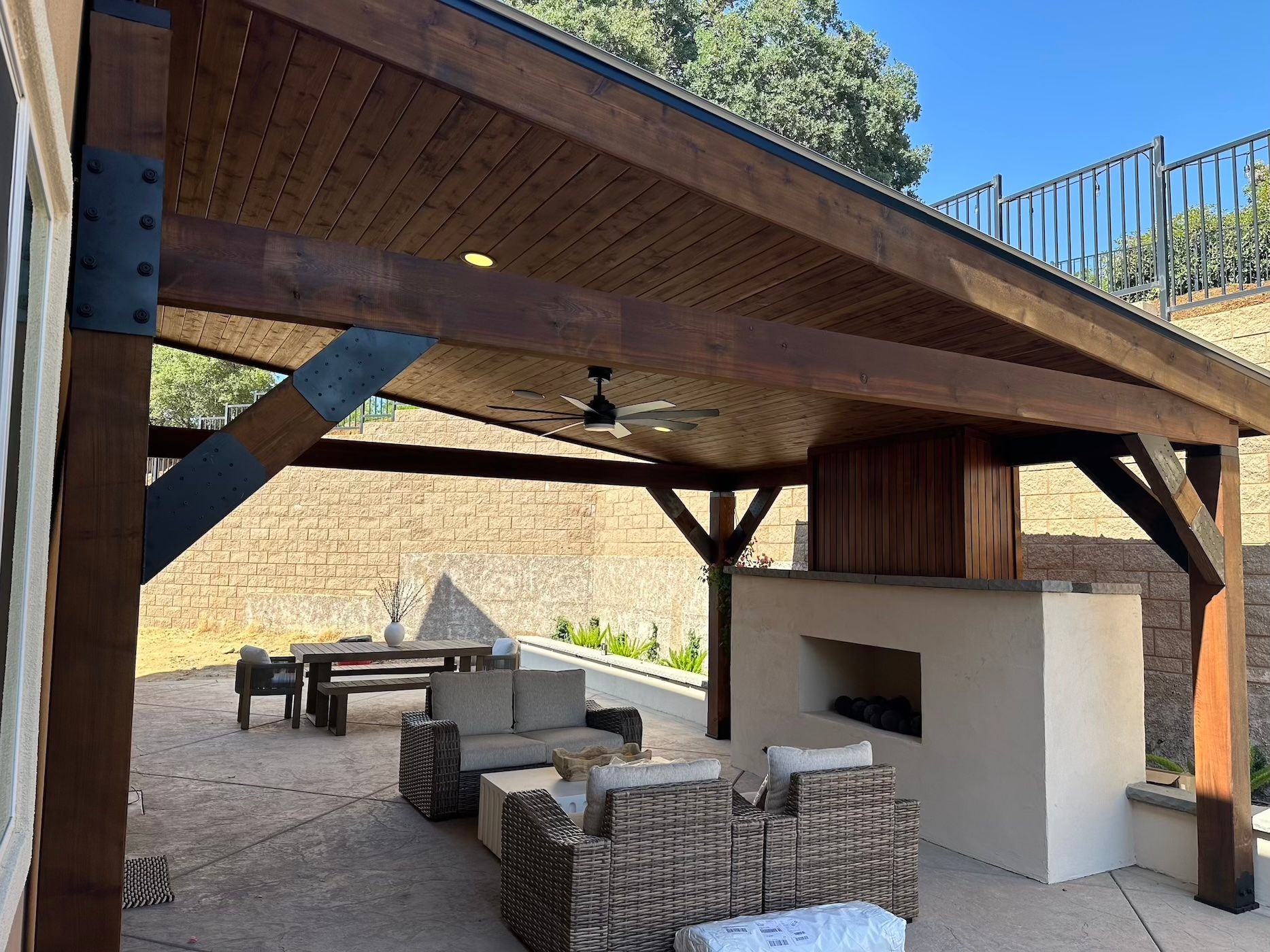 A wooden pavilion with wicker furniture and a fireplace underneath it.