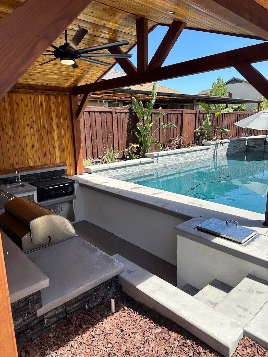 There is a swimming pool in the backyard with a ceiling fan.