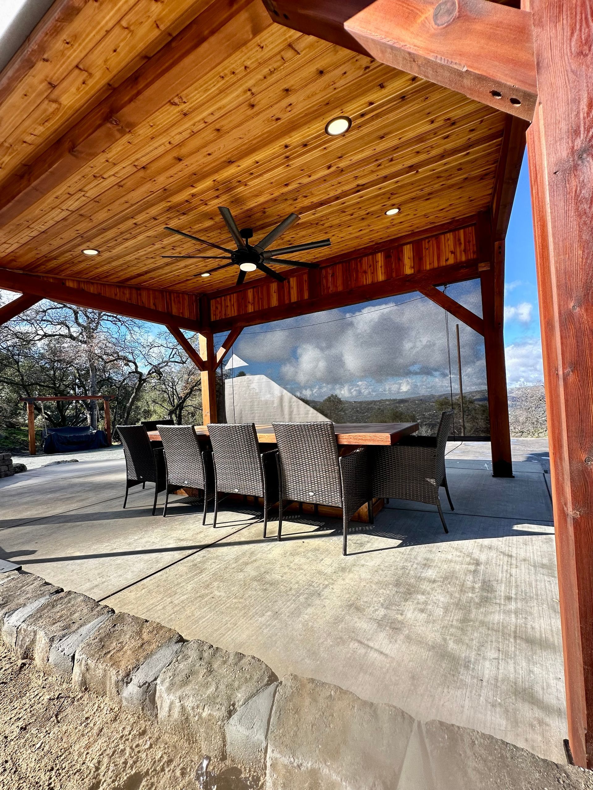 a wooden pavilion with a ceiling fan and a table and chairs underneath it .