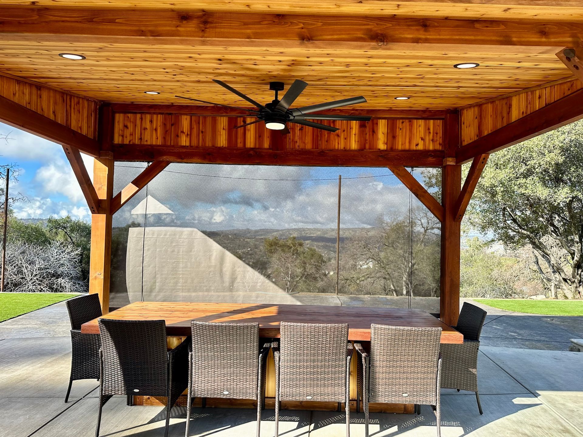a table and chairs under a wooden structure with a ceiling fan