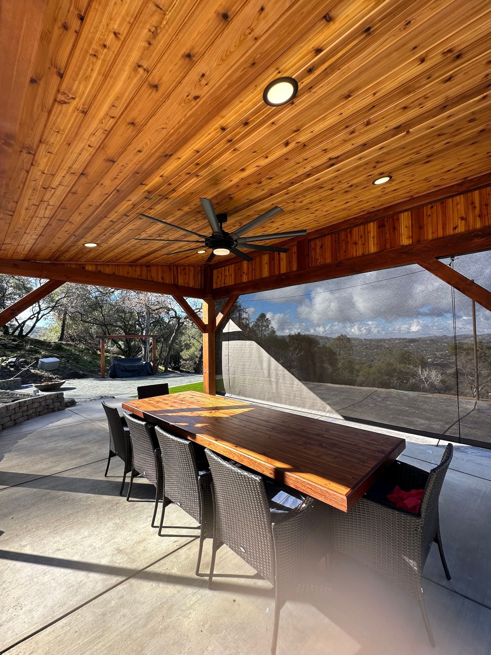 a patio with a table and chairs under a wooden roof with a ceiling fan .