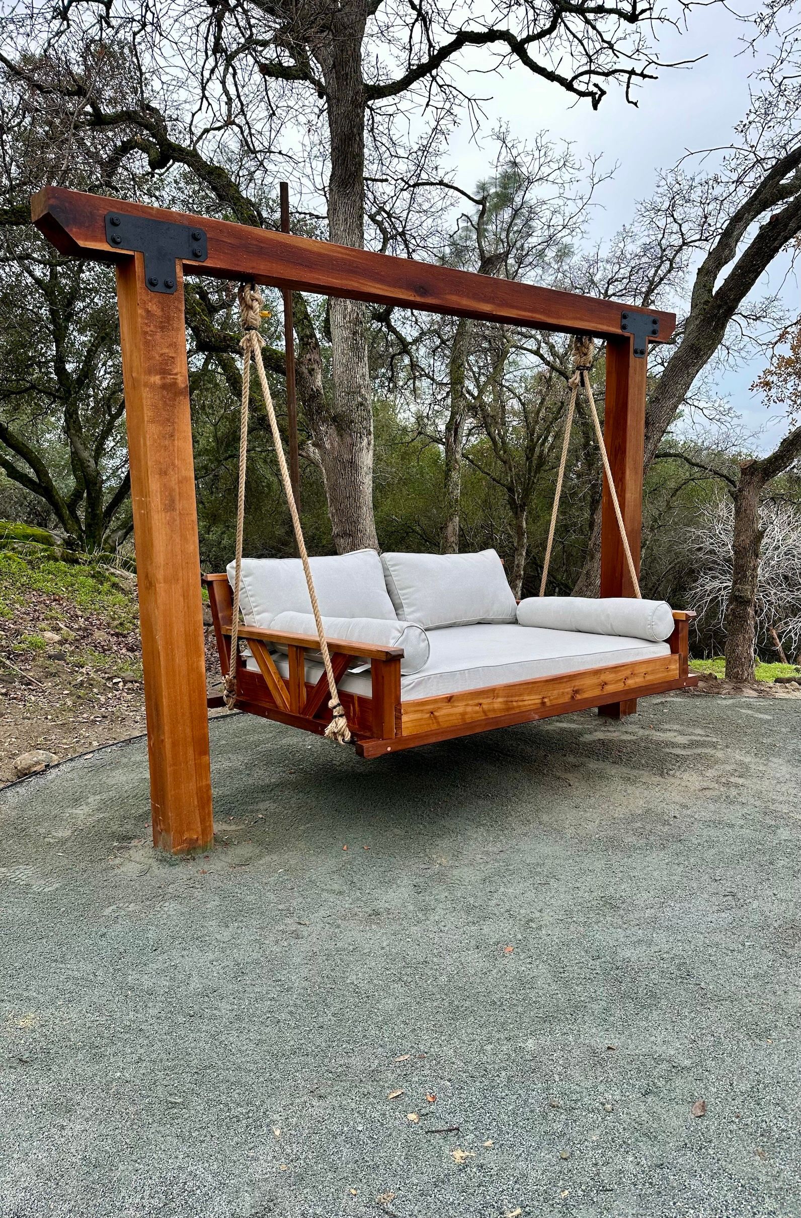 a wooden porch swing with white cushions is hanging from a wooden post .