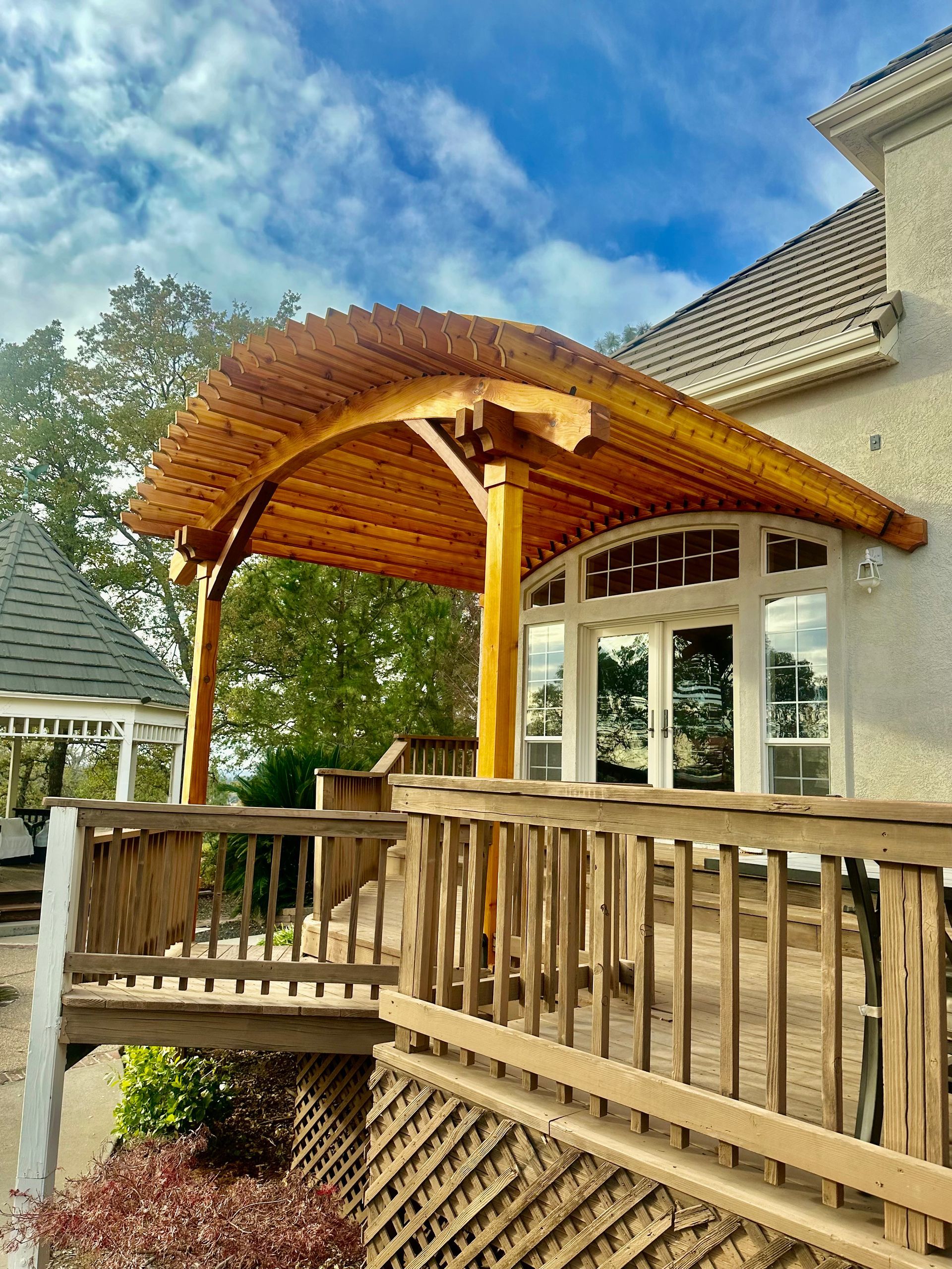 A wooden gazebo is sitting on top of a wooden deck next to a house.