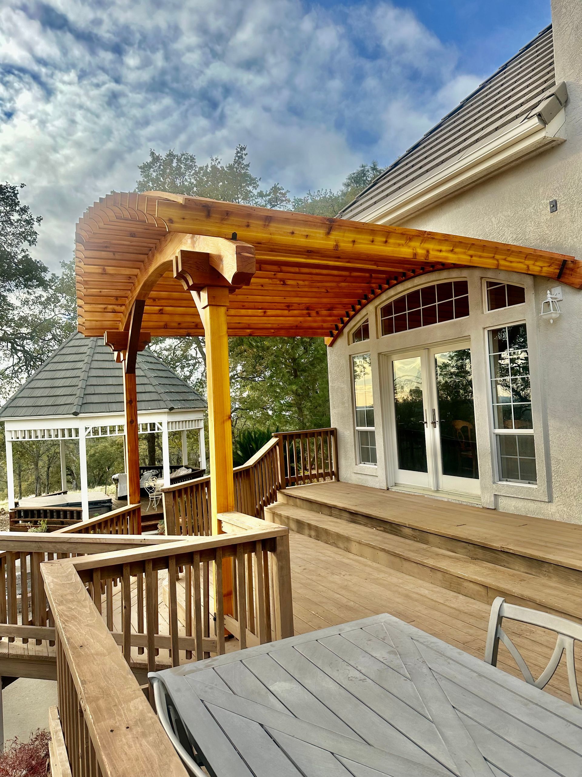 A wooden pergola is sitting on top of a deck next to a house.