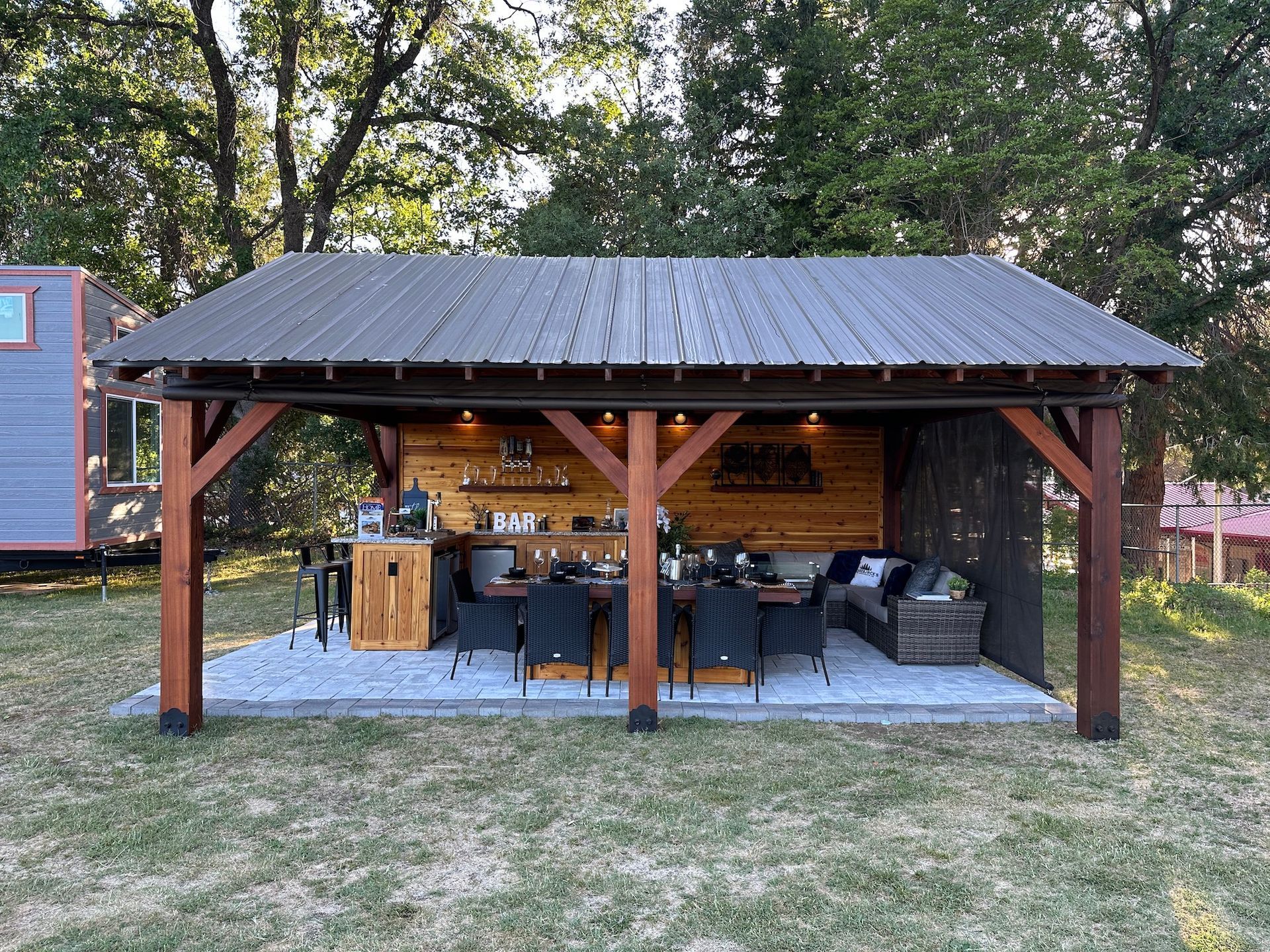 A large wooden pavilion with a metal roof and a table and chairs underneath it.