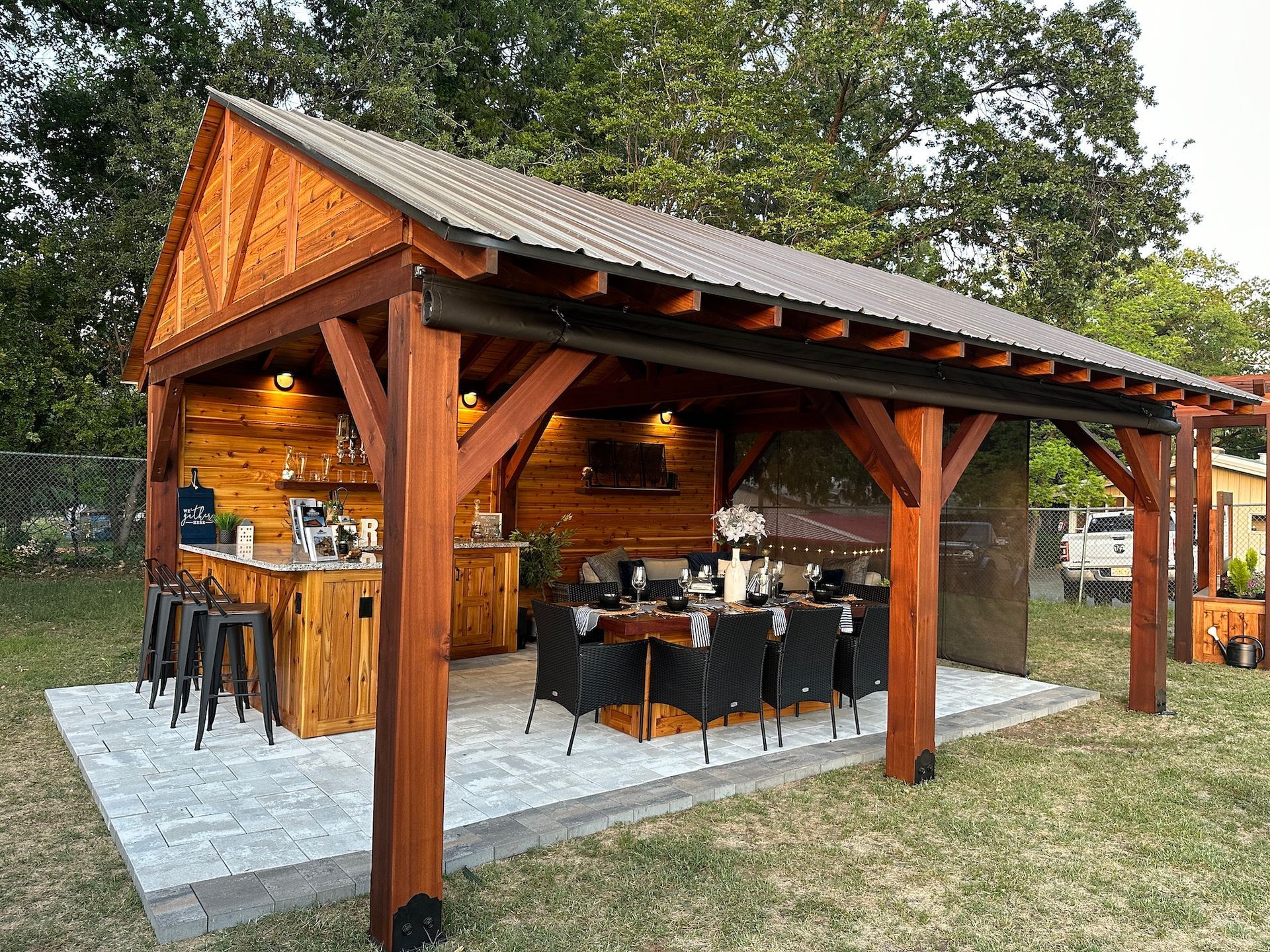 A wooden pavilion with a table and chairs underneath it in a backyard.