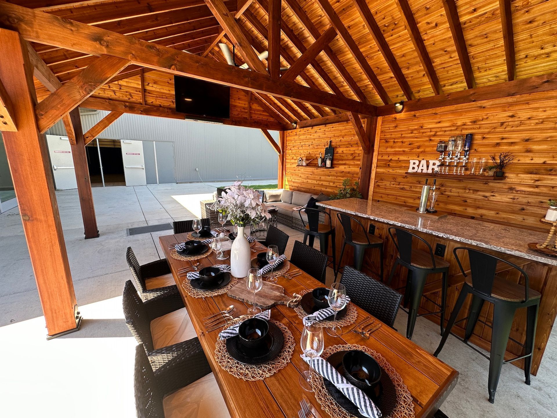 A large wooden table and chairs under a wooden roof.