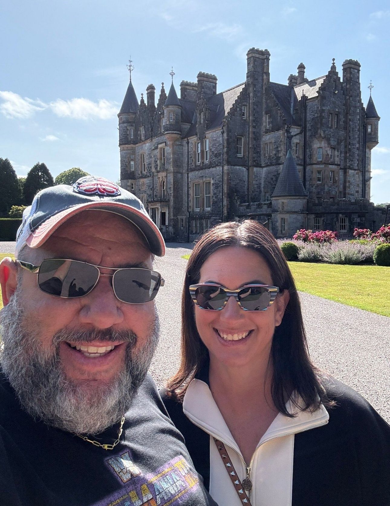 Couple poses in front of the Rock of Cashel ruins in Ireland on a sunny day.