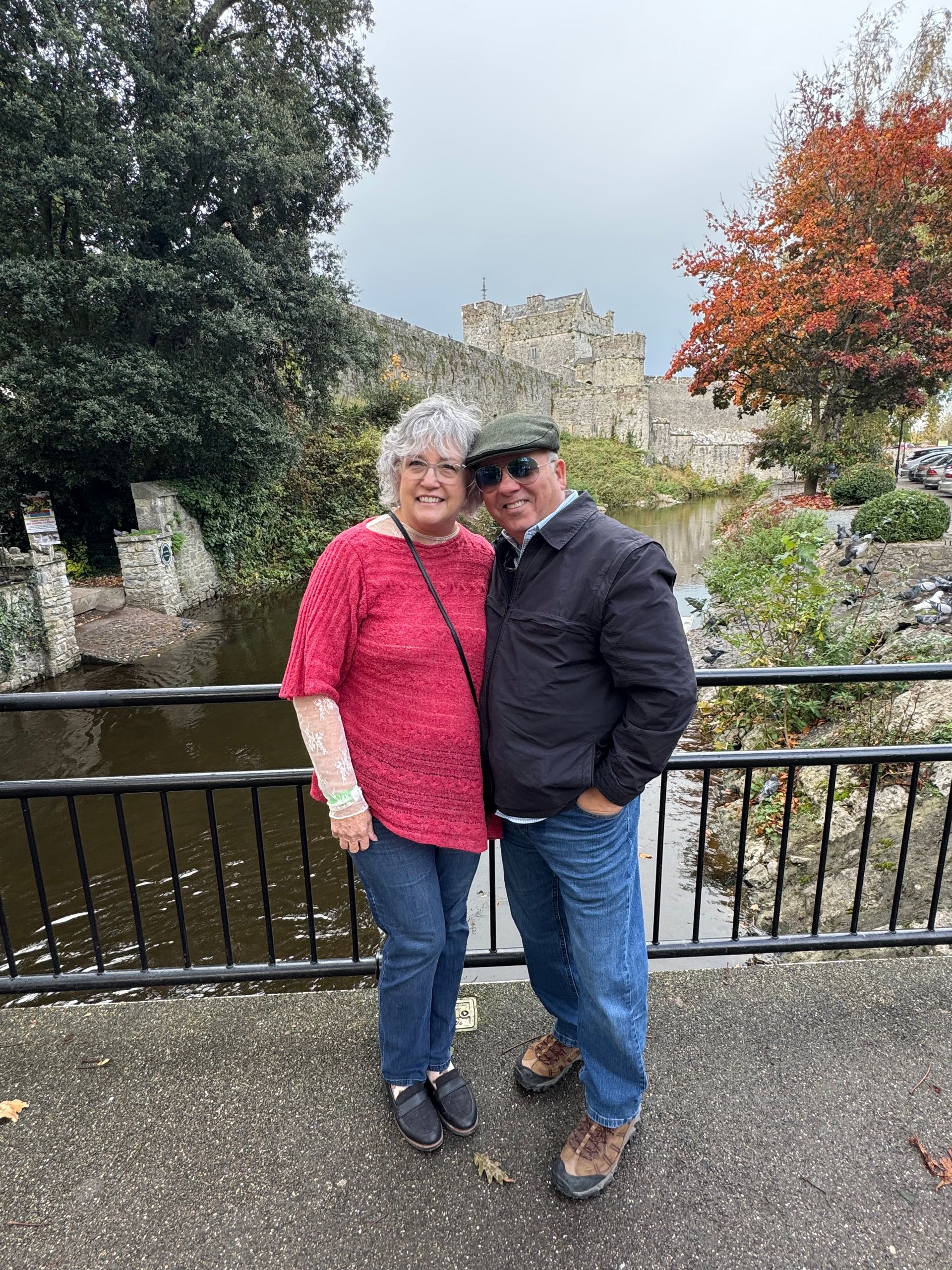 Three people smiling in front of a marina with boats on a sunny day.