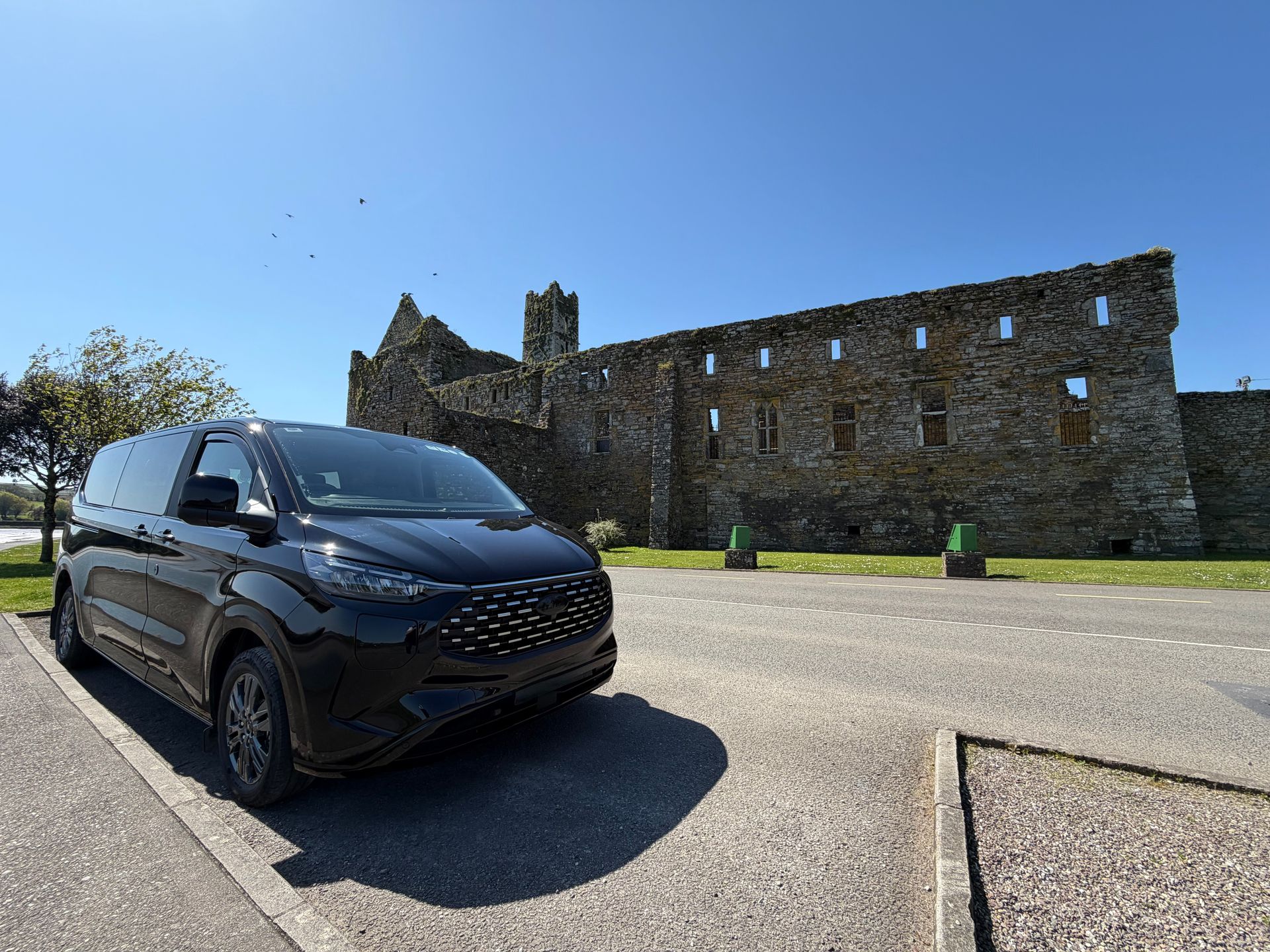 Executive touring vehicle parked in front of a stone castle ruin on a sunny day