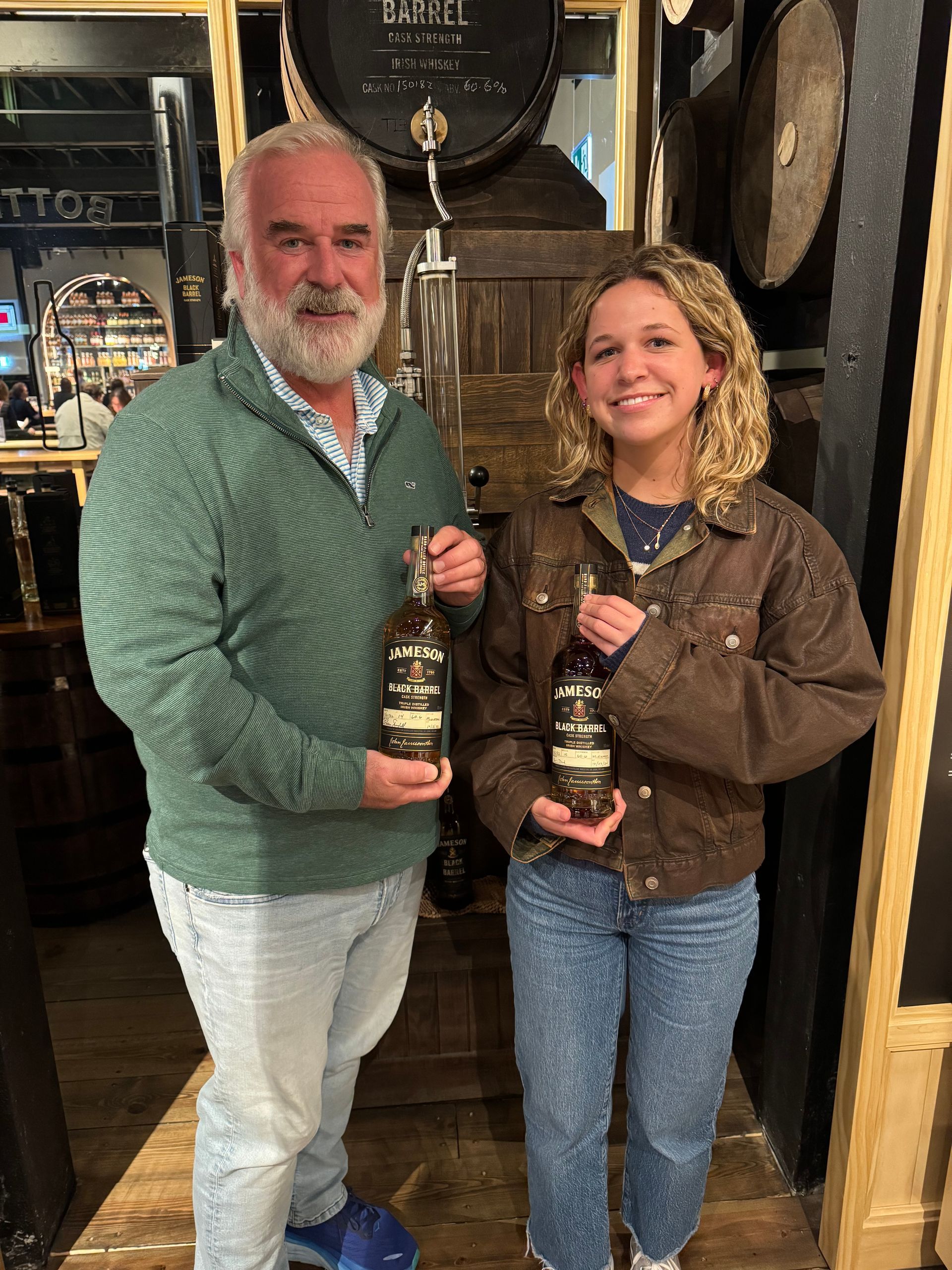 Two people holding bottles of Jameson in a rustic shop doorway, smiling at the camera.
