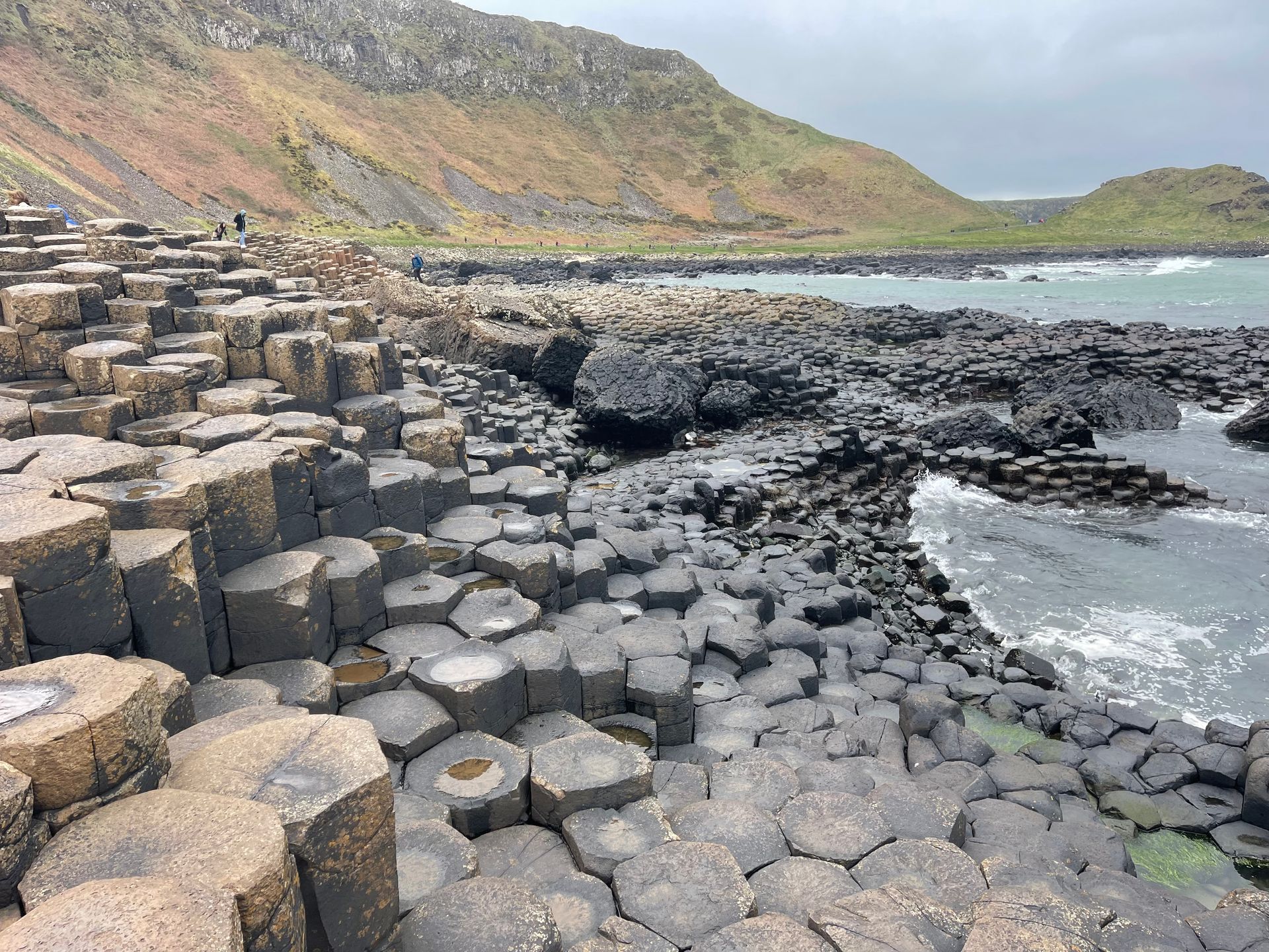 Hexagonal basalt columns form a shoreline at the Giant's Causeway in Northern Ireland, with a coastal mountain in the background.