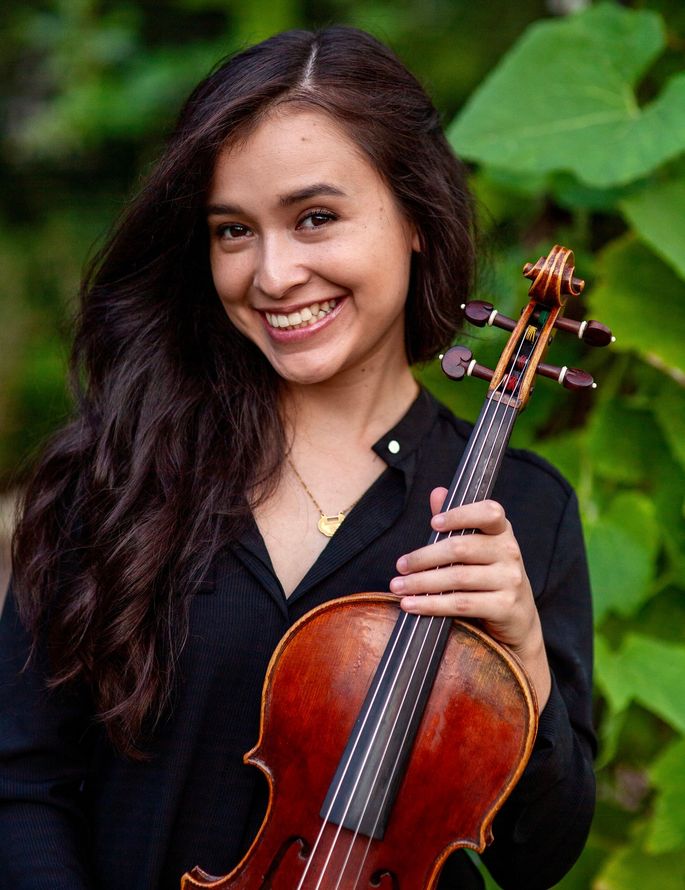 A woman in a black shirt is holding a violin and smiling.