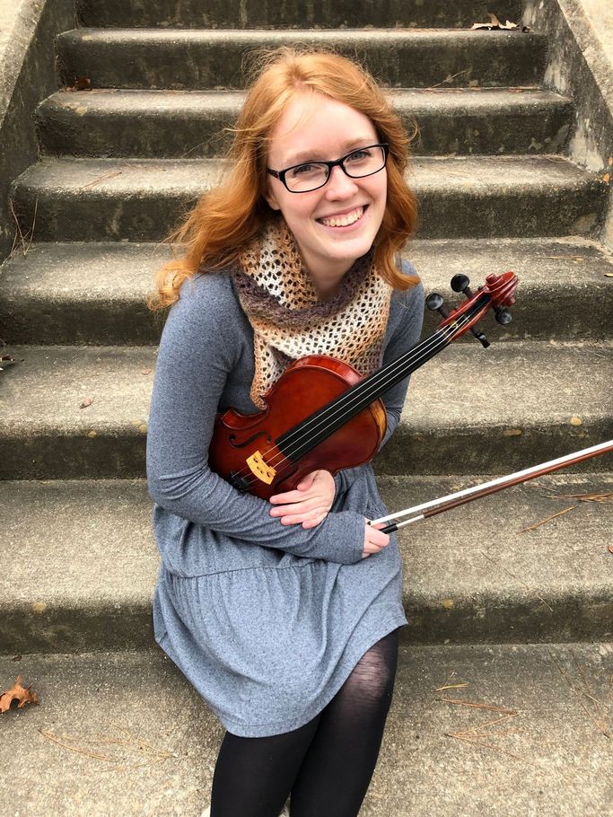 A young woman is sitting on a set of stairs holding a violin.