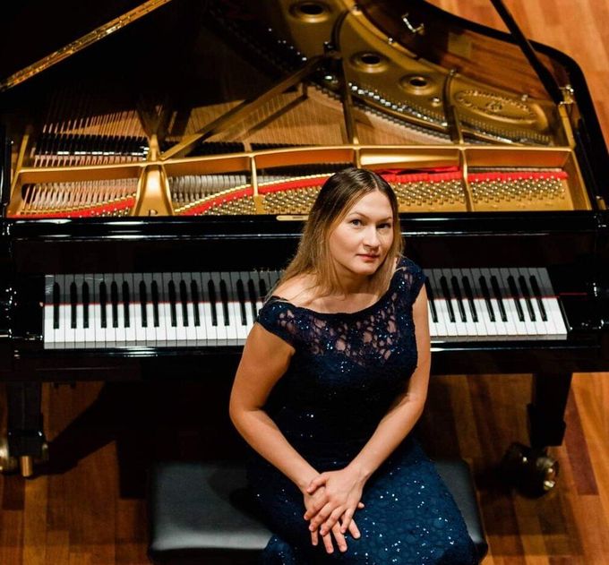 A woman in a blue dress is sitting in front of a piano